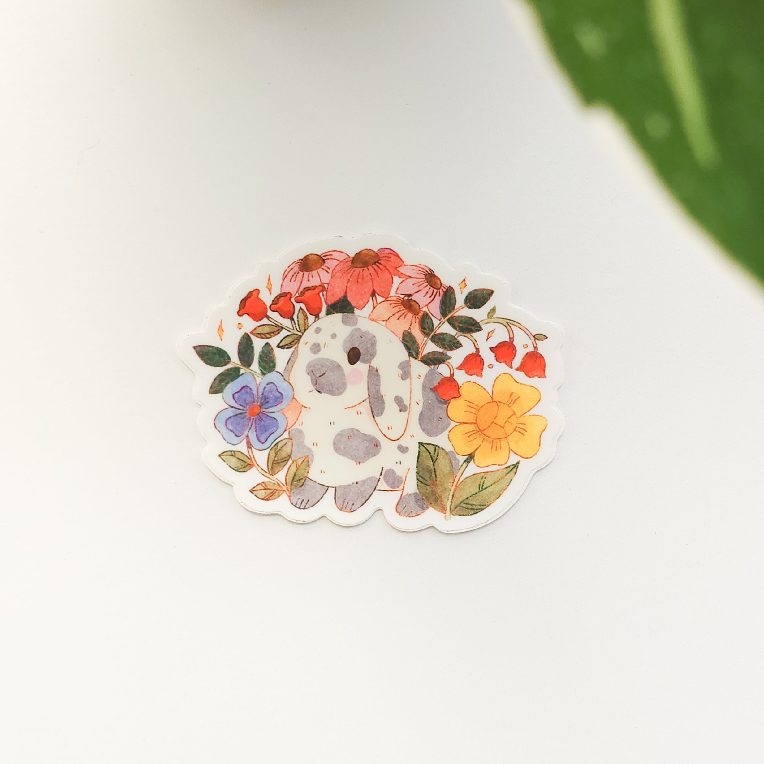 sticker of a gray and white rabbit in a garden of flowers on a white background with a leaf
