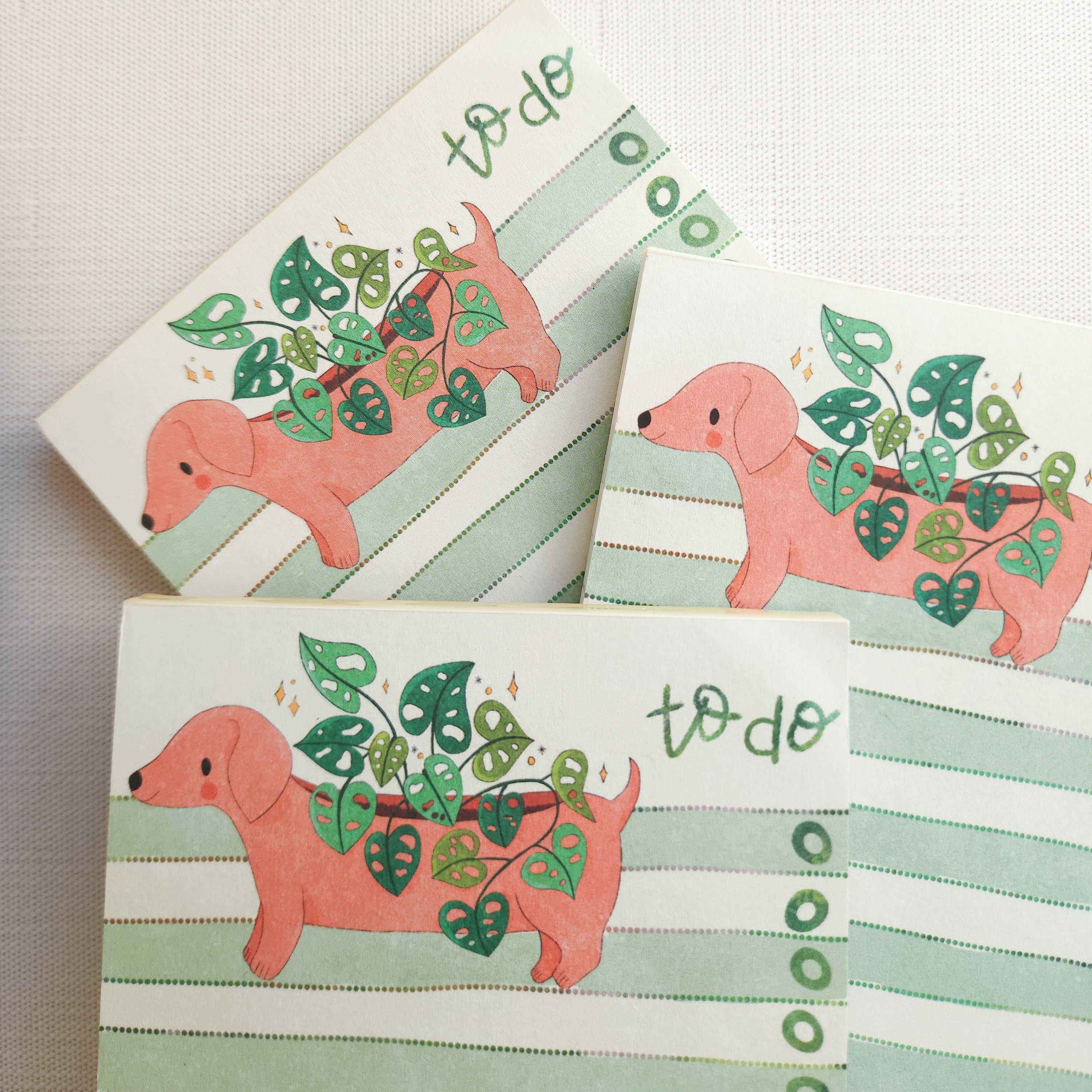 3 notepads with dachshund illustrations and green stripes stacked on each other on a neutral background