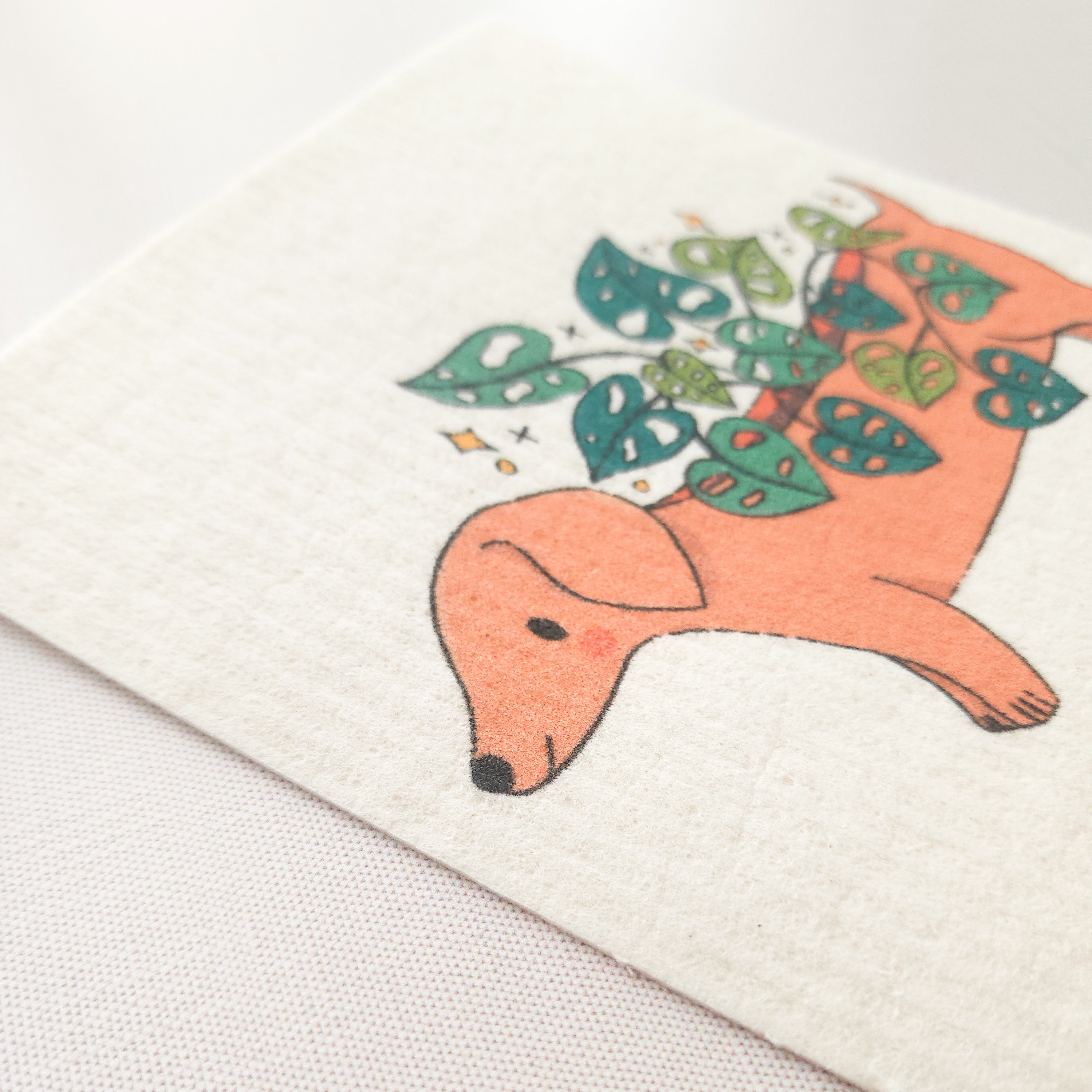 close up image of a swedish dishcloth with an illustration of a dachshund planter growing a cheese plant, to show the texture of the cloth