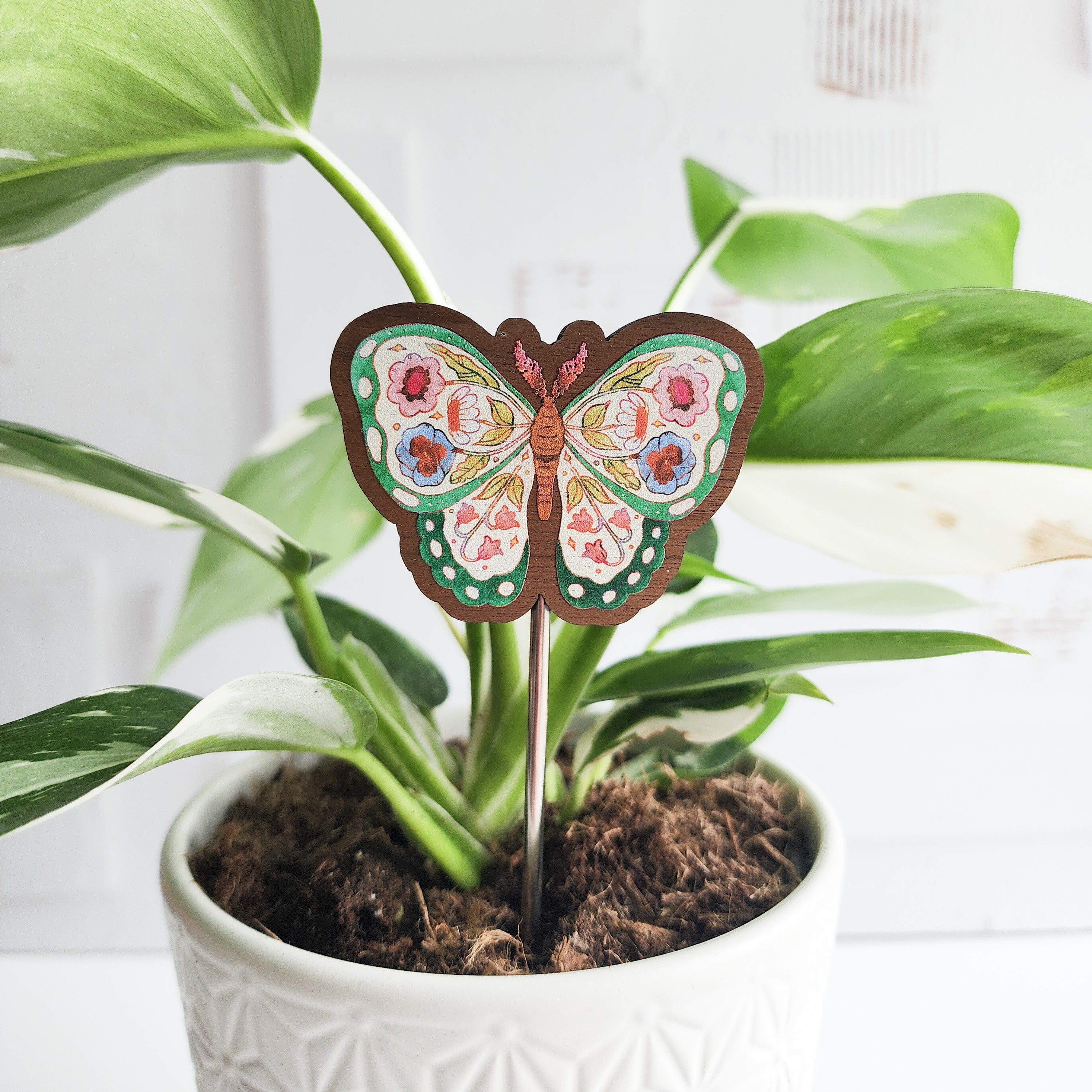Decorative butterfly plant stake in a pot with green leaves