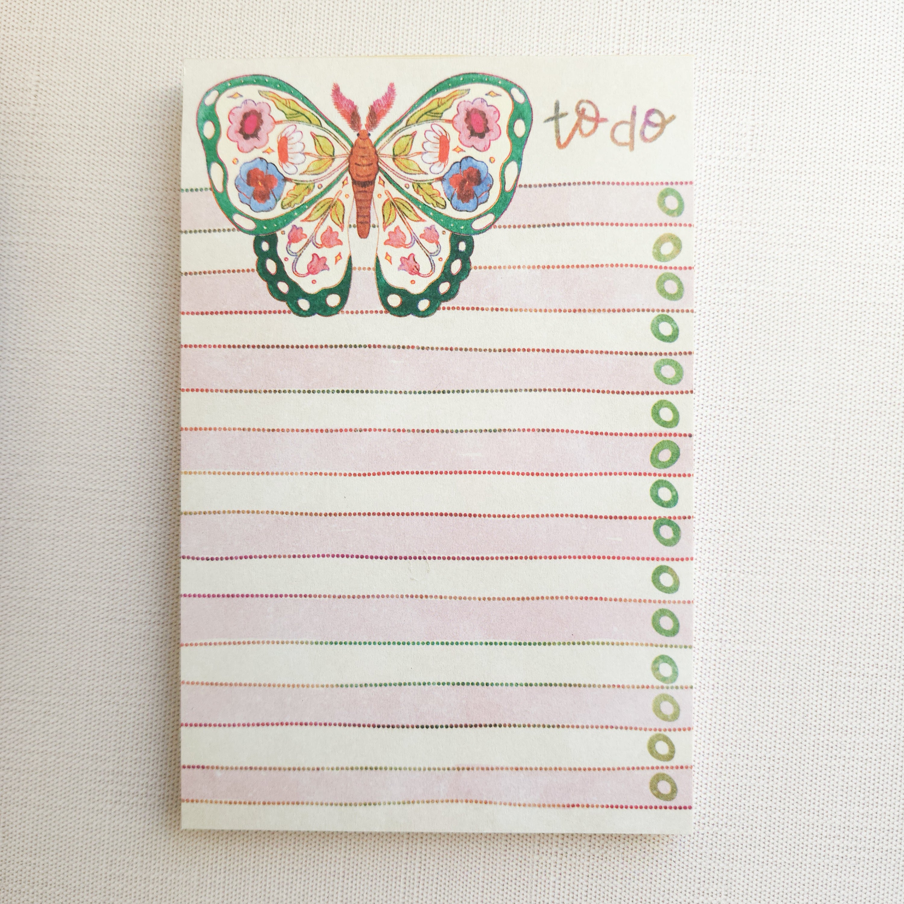 notepad with an illustrated floral butterfly and pink stripes on a neutral background