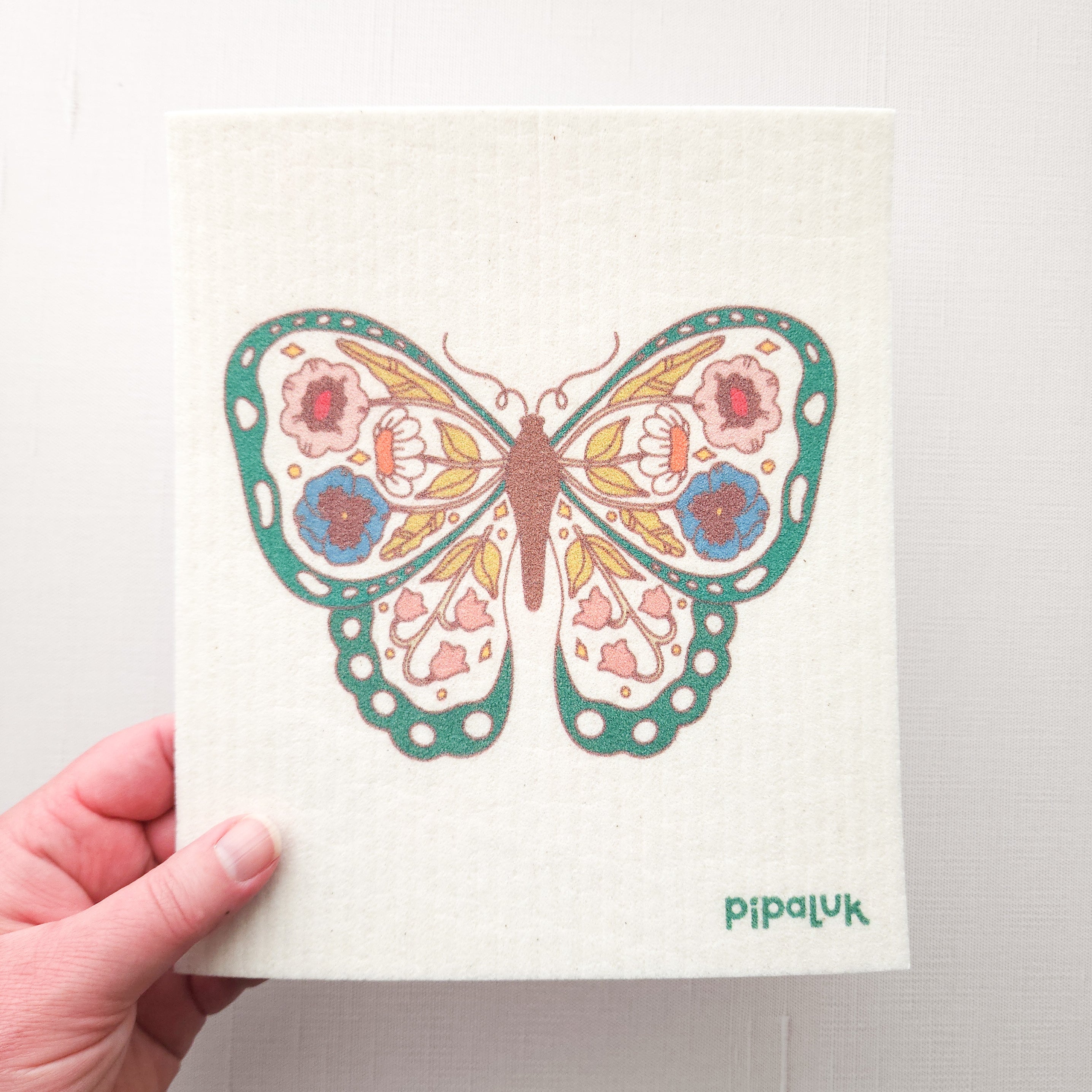 swedish dishcloth with a green, floral, butterfly design held in a hand on a white background