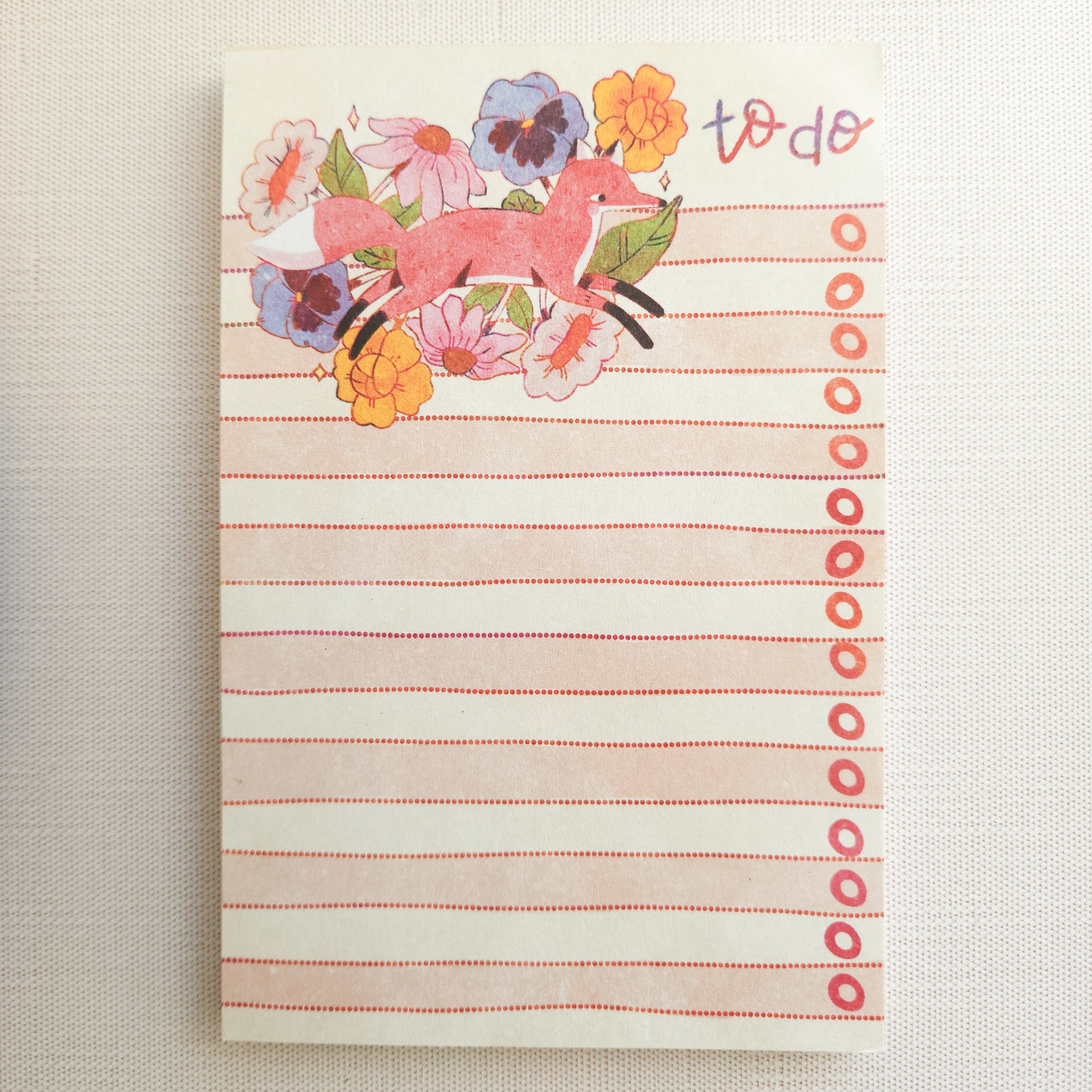 notepad with an illustration of a fox jumping through flowers on a neutral background
