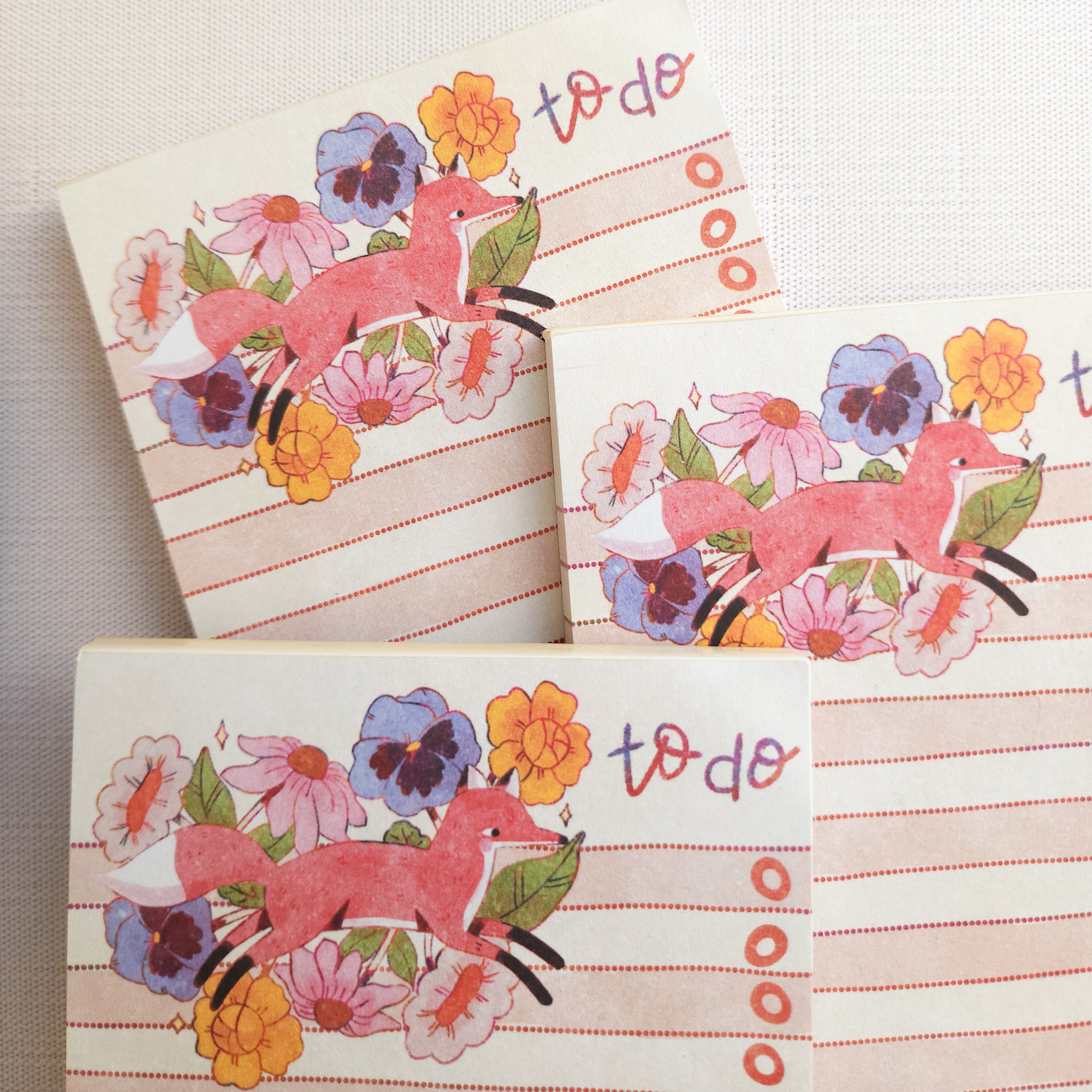 Set of three noteapads with fox and floral designs on a beige background