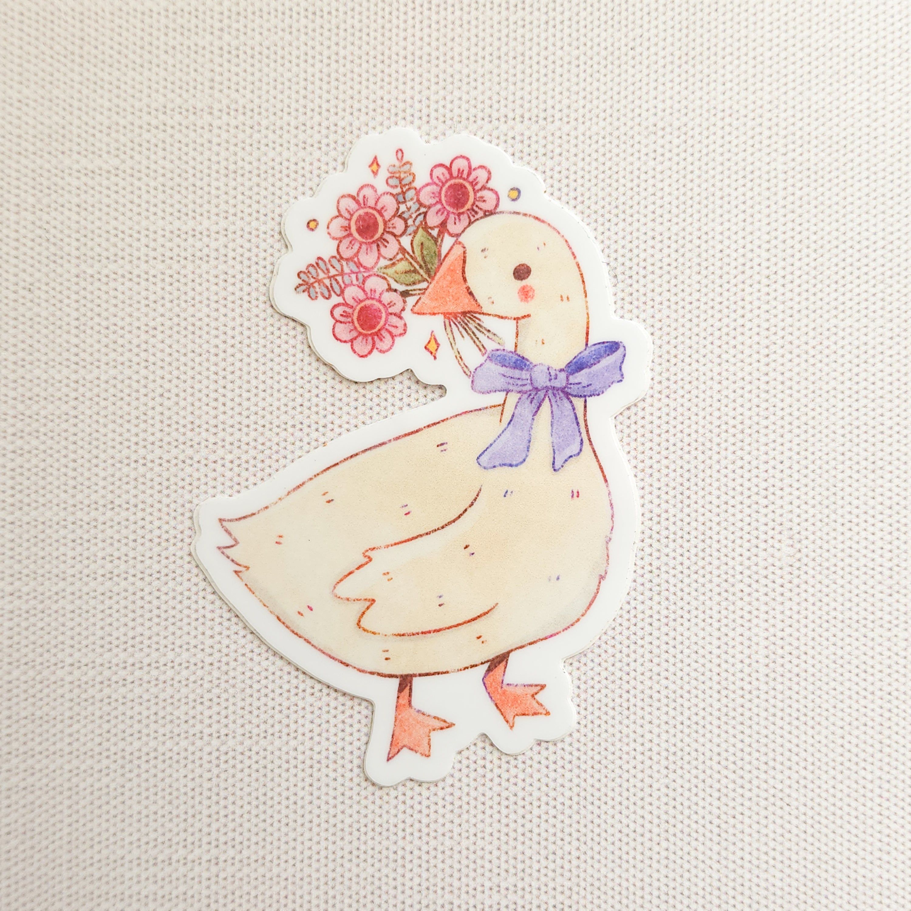 sticker with an illustration of a goose holding a bouquet of flowers on a linen background