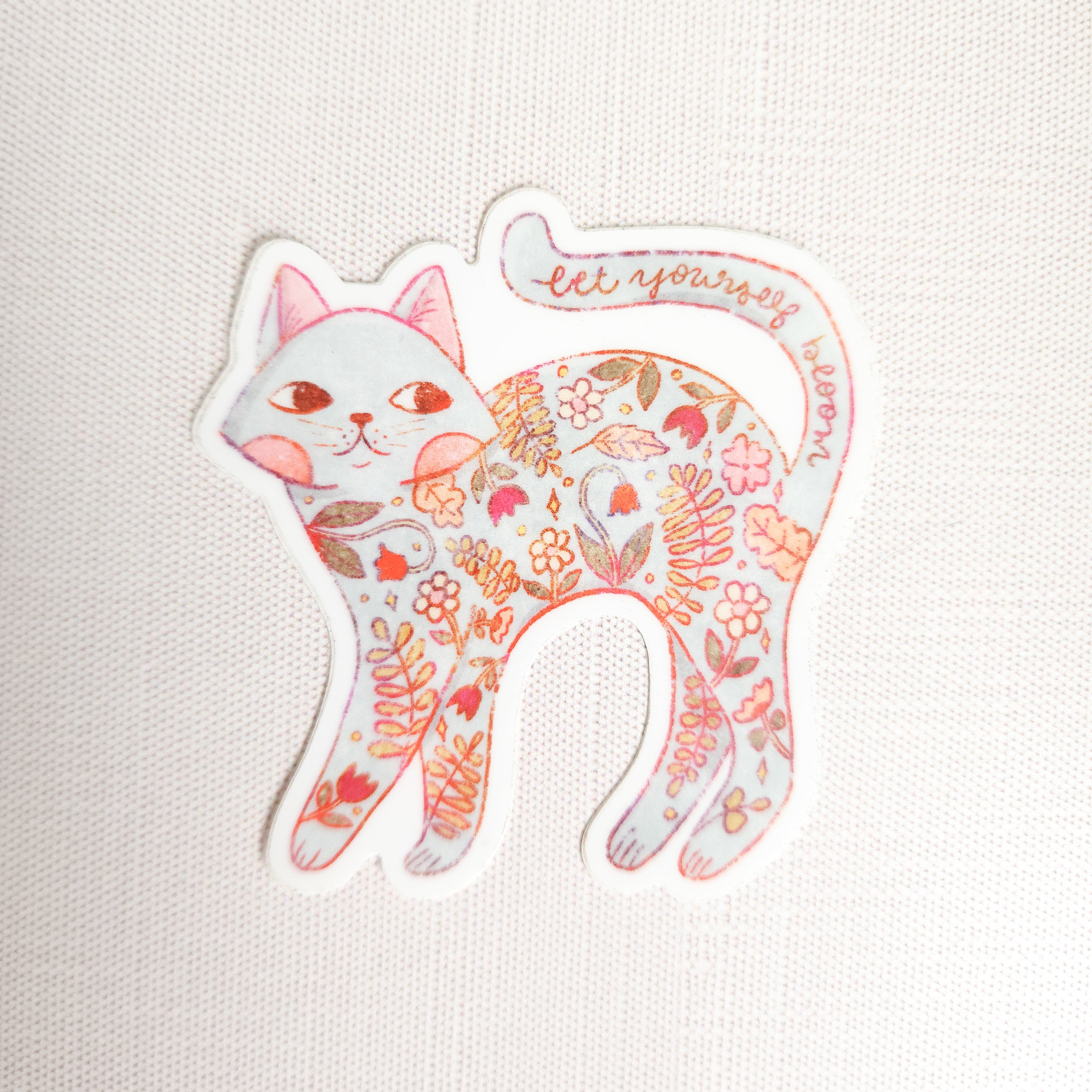 sticker of a floral cat with the words let yourself bloom on a linen background