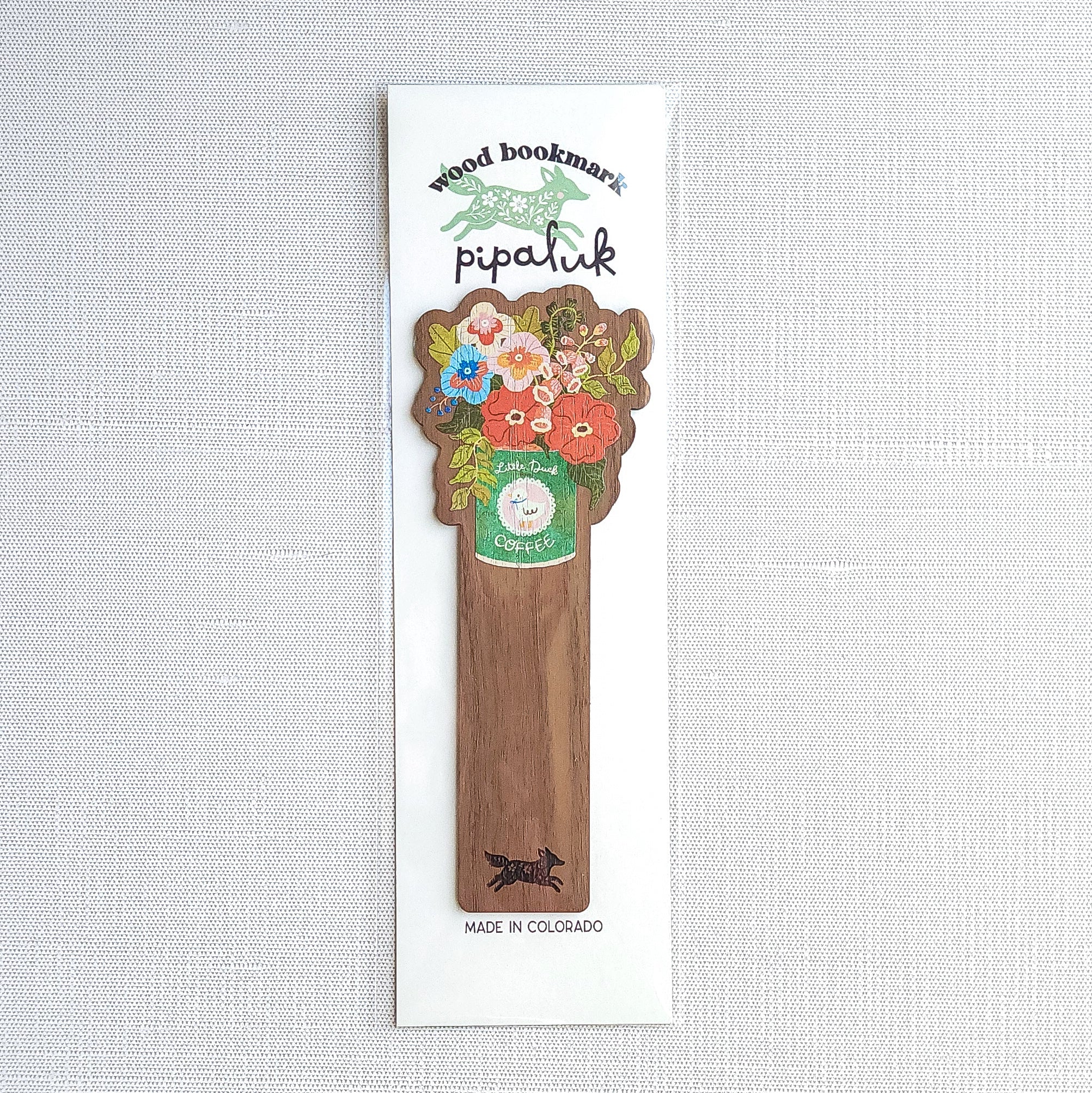 Walnut wood bookmark with a vintage-inspired Little Duck Coffee can filled with cheerful pink, yellow, and blue garden blooms in Pipaluk branded packaging on a neutral background