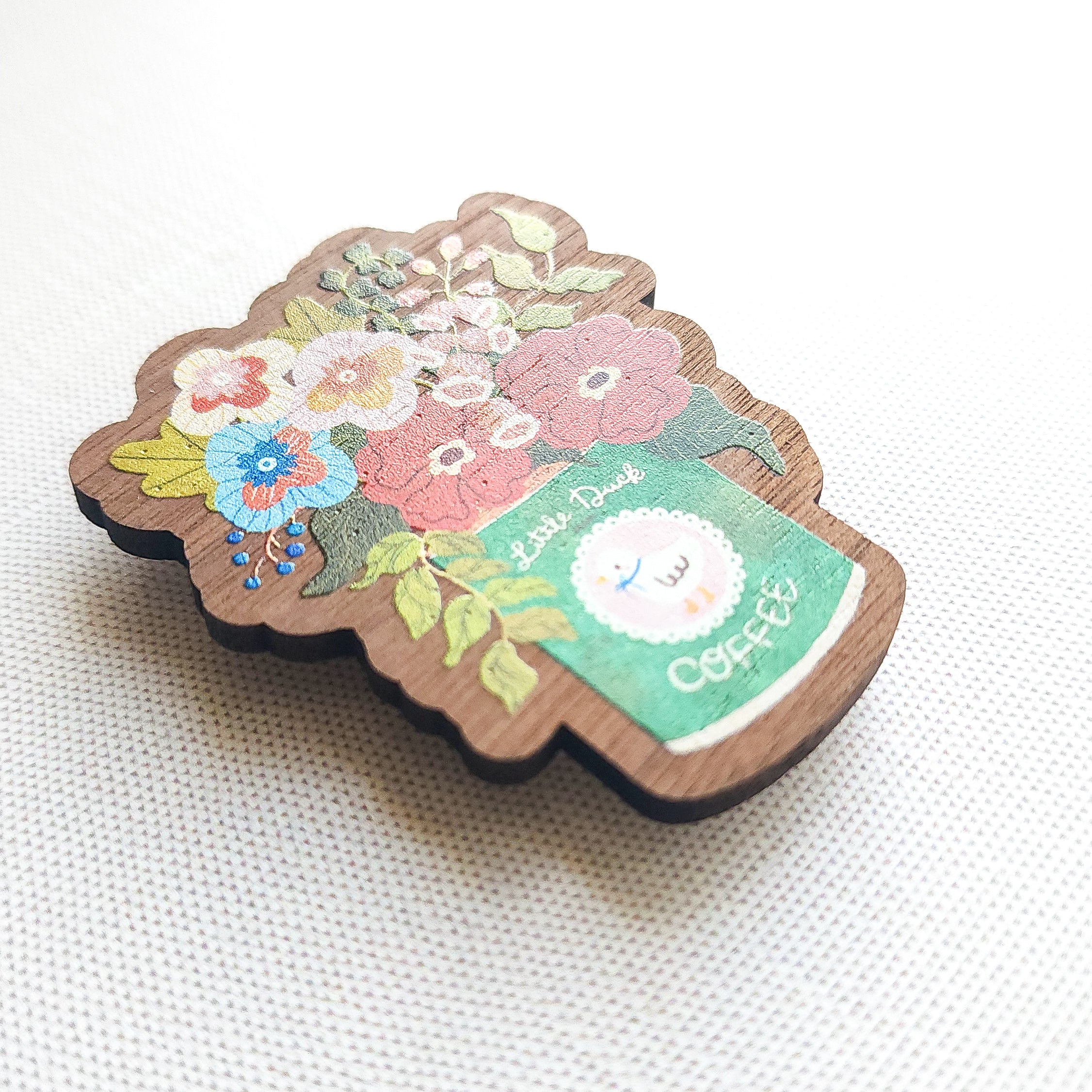 Wooden magnet with an illustrated Little Duck Coffee can repurposed as a vase, filled with cheerful pink, yellow, and blue flowers on a neutral background