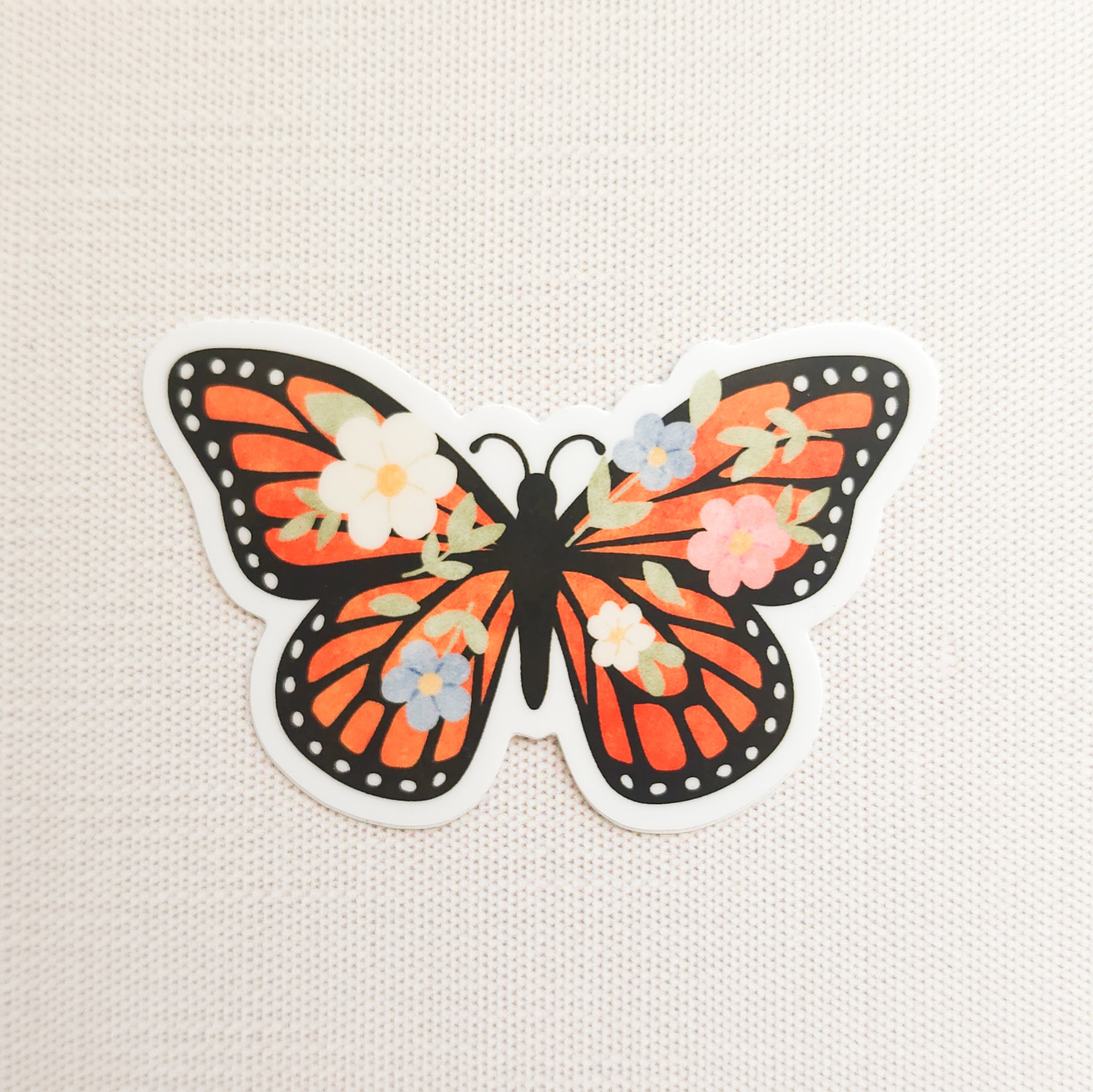 sticker with an illustration of a monarch butterfly with flowers in its wings on a linen background