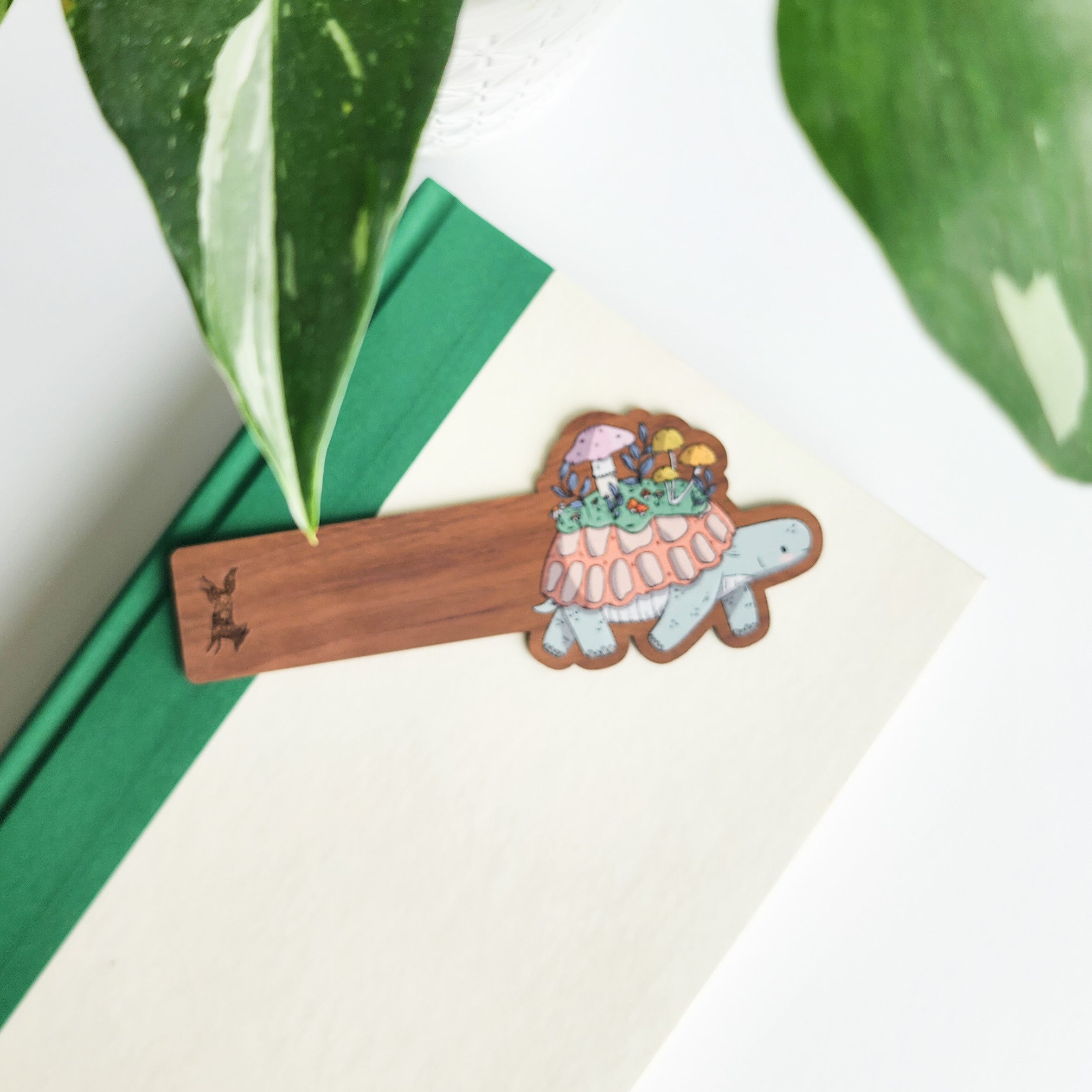 Wooden bookmark with a turtle design on a white surface with green leaves in the background