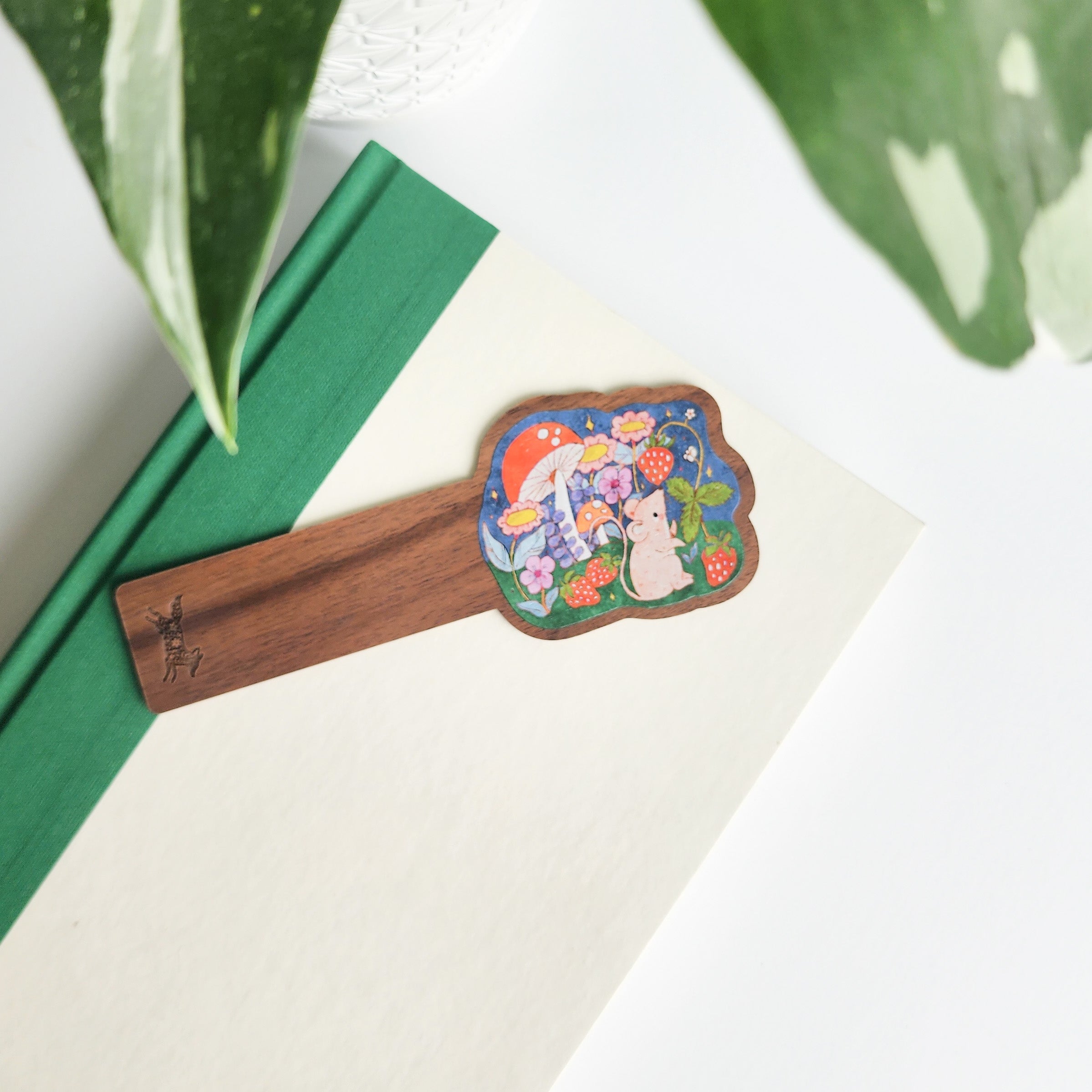 mouse bookmark on a green and white book on a white background with leaves