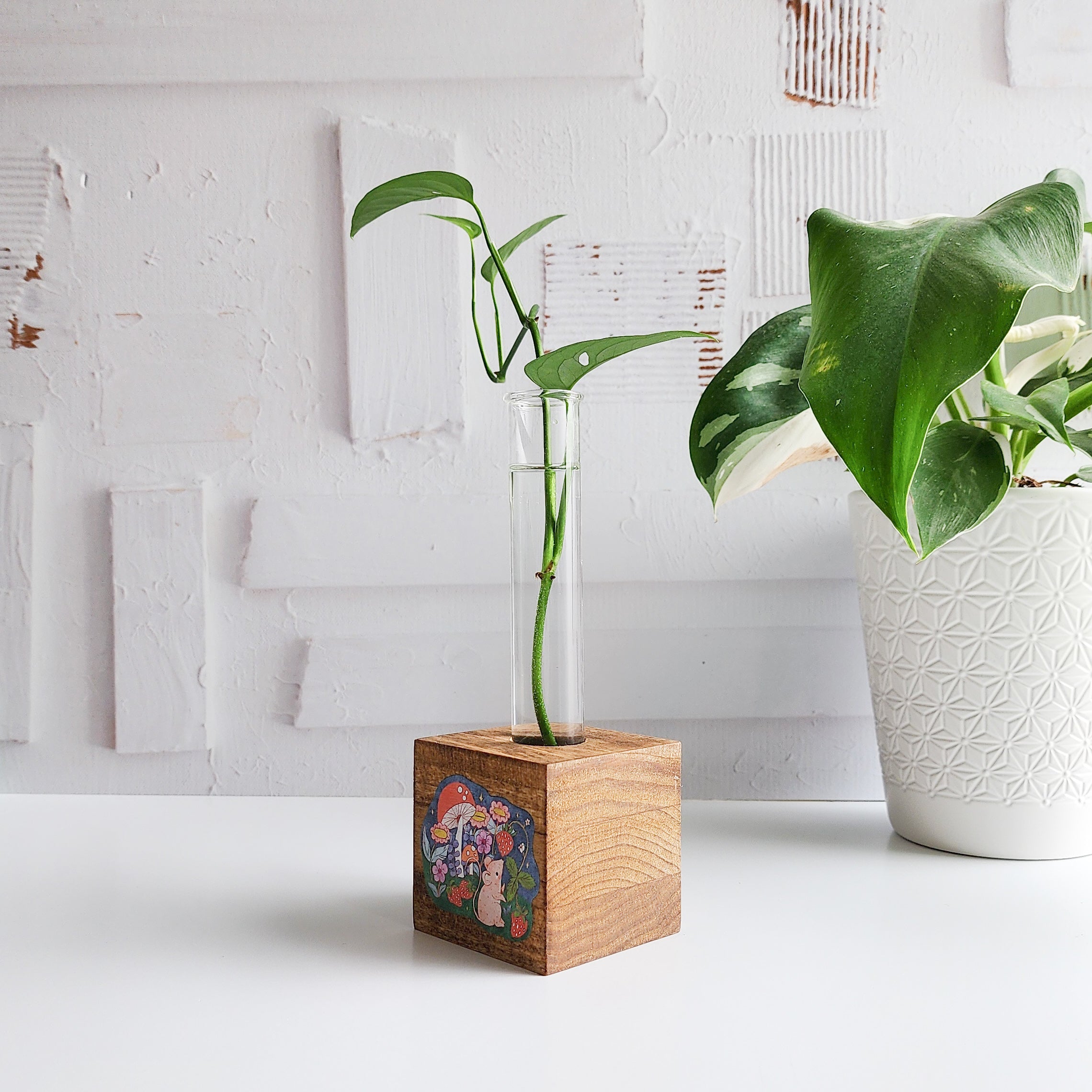 wooden propagation station with a mouse picking strawberries. There is a green plant cutting in a glass tube on a white background
