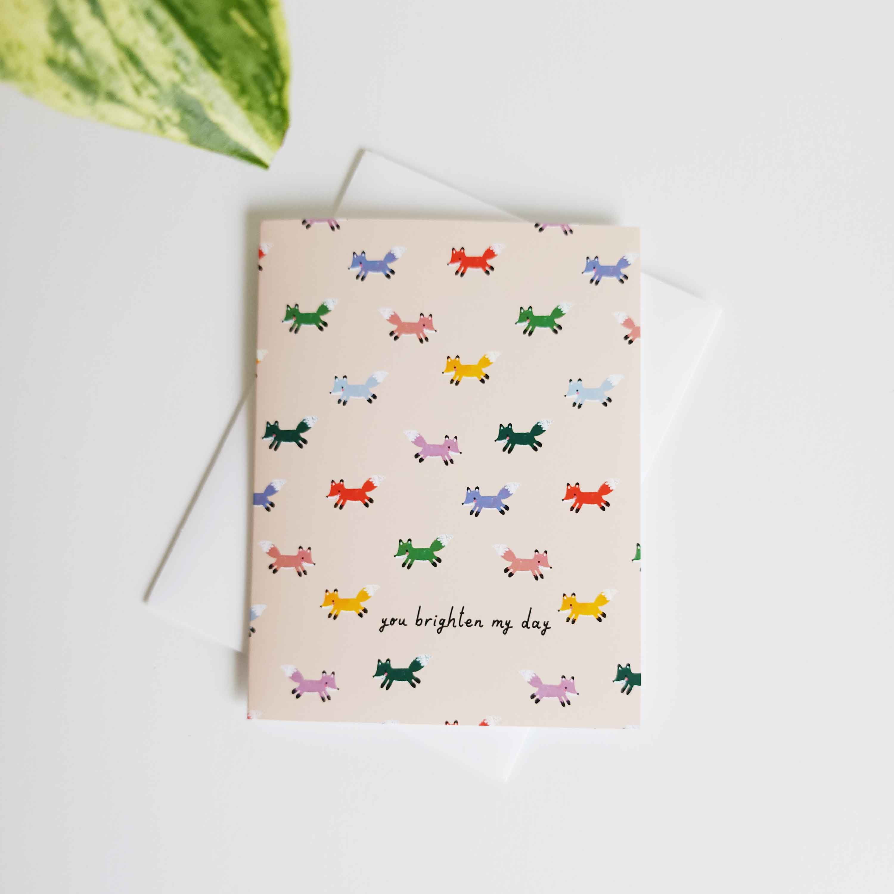 cream card with multi colored foxes and the words you brighten my day
