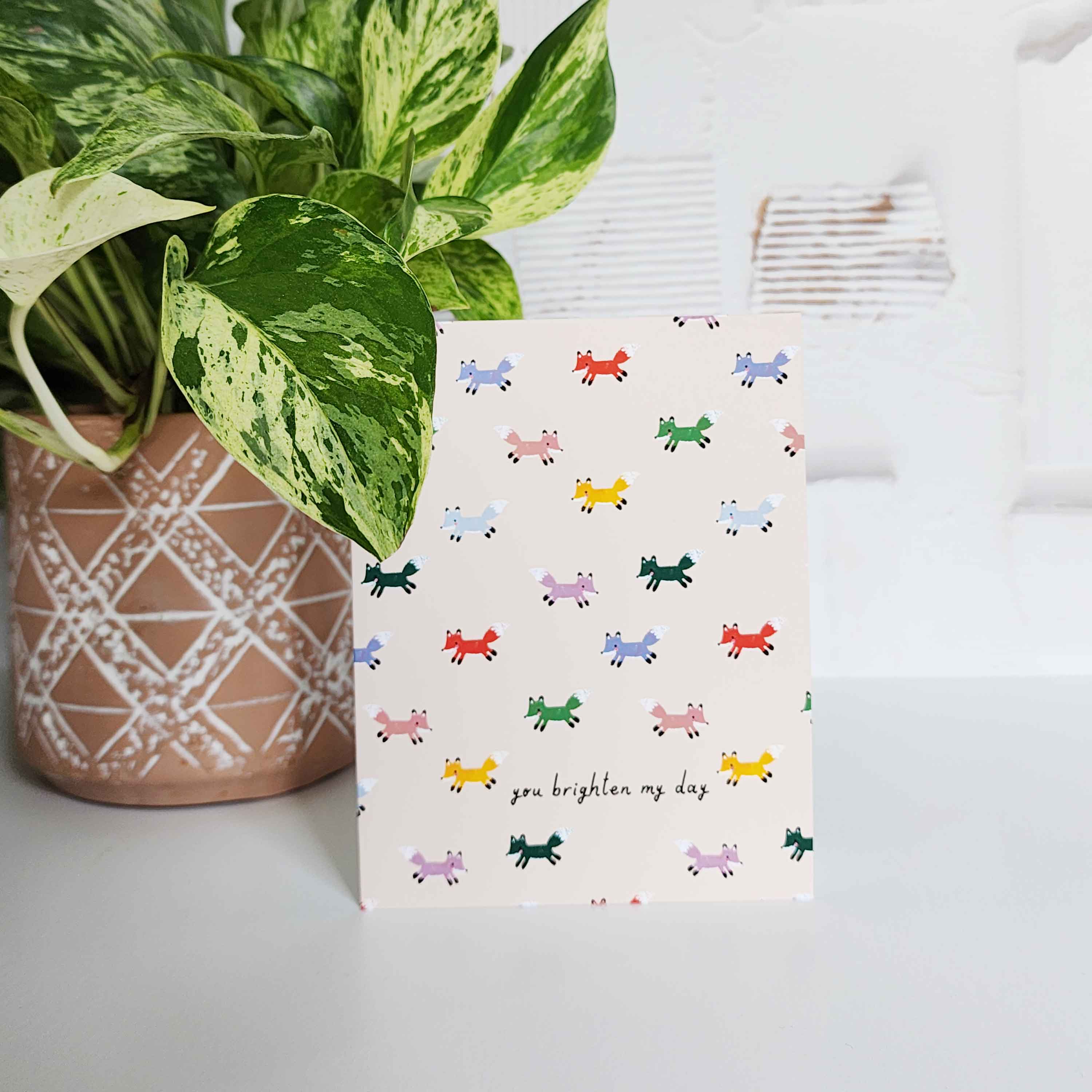 cream card with multi colored foxes and the words you brighten my day