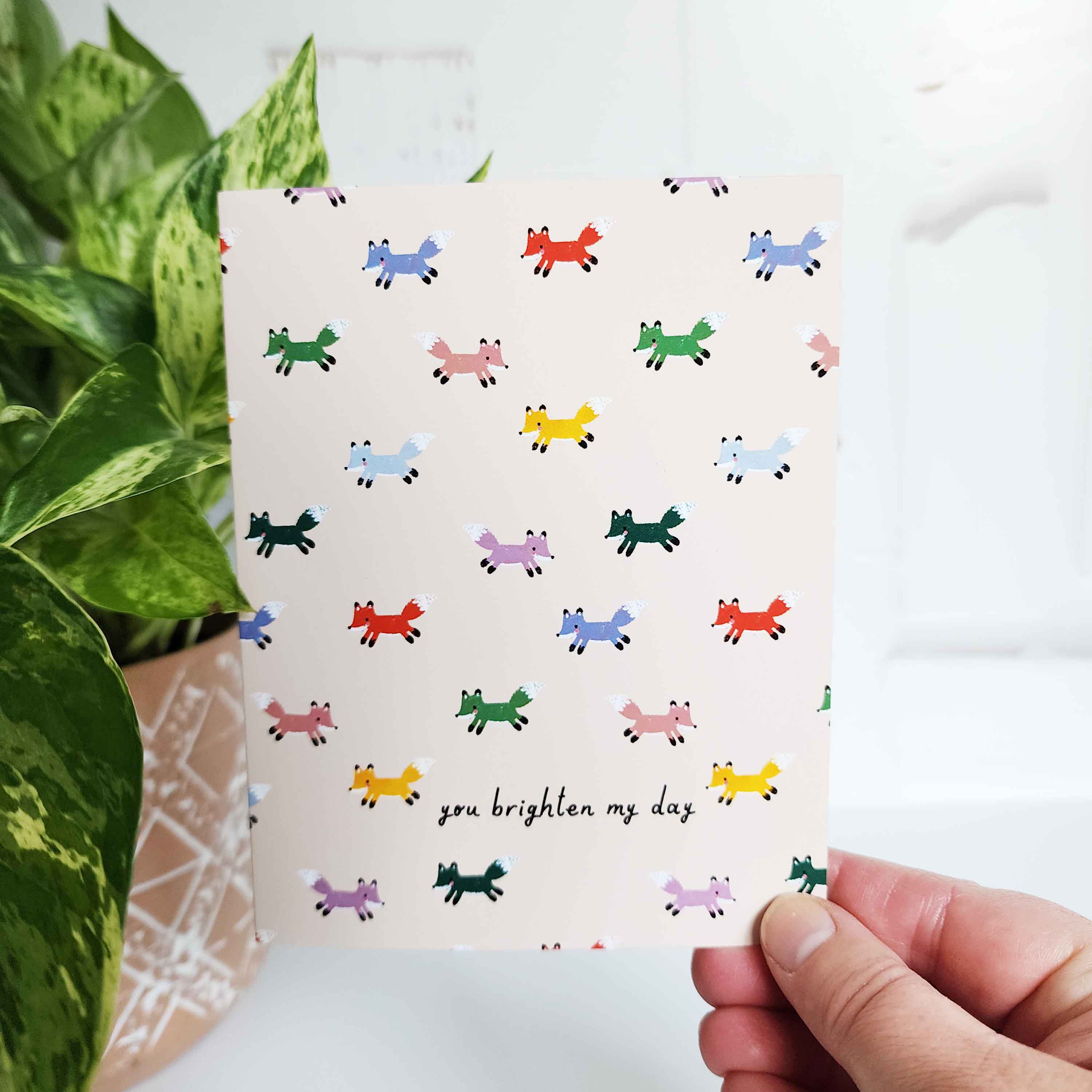 cream card with multi colored foxes and the words you brighten my day