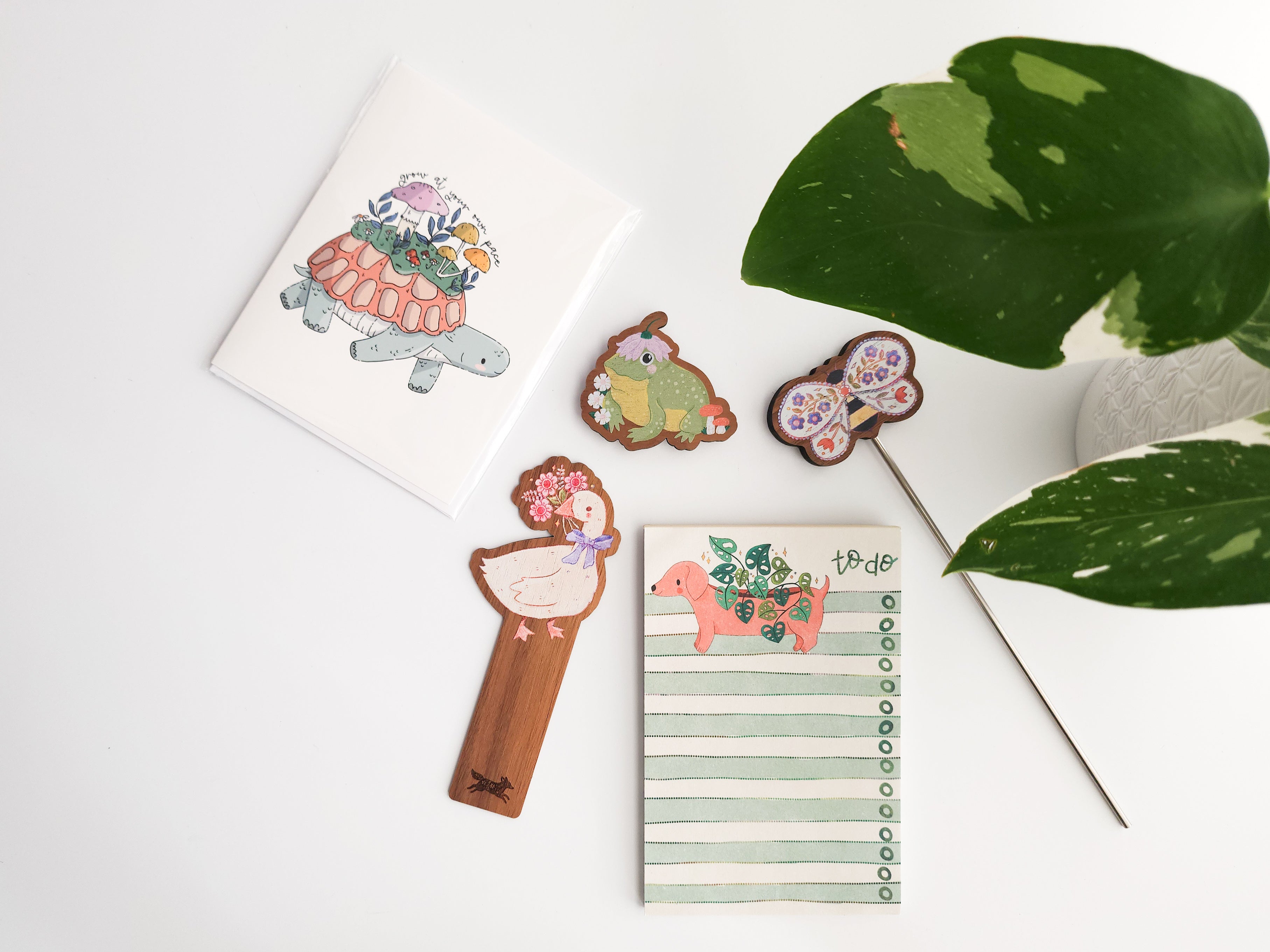 Decorative cards bookmarks, and a notepad with animal illustrations on a white surface with green leaves.