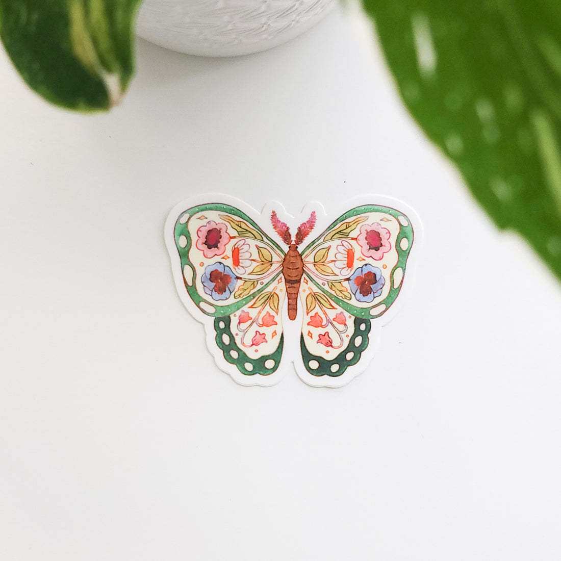 colorful butterfly sticker with flowers on a white background next to a plant