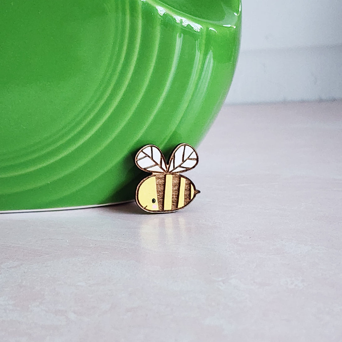 yellow wooden bee pin sitting in fron of a green vase