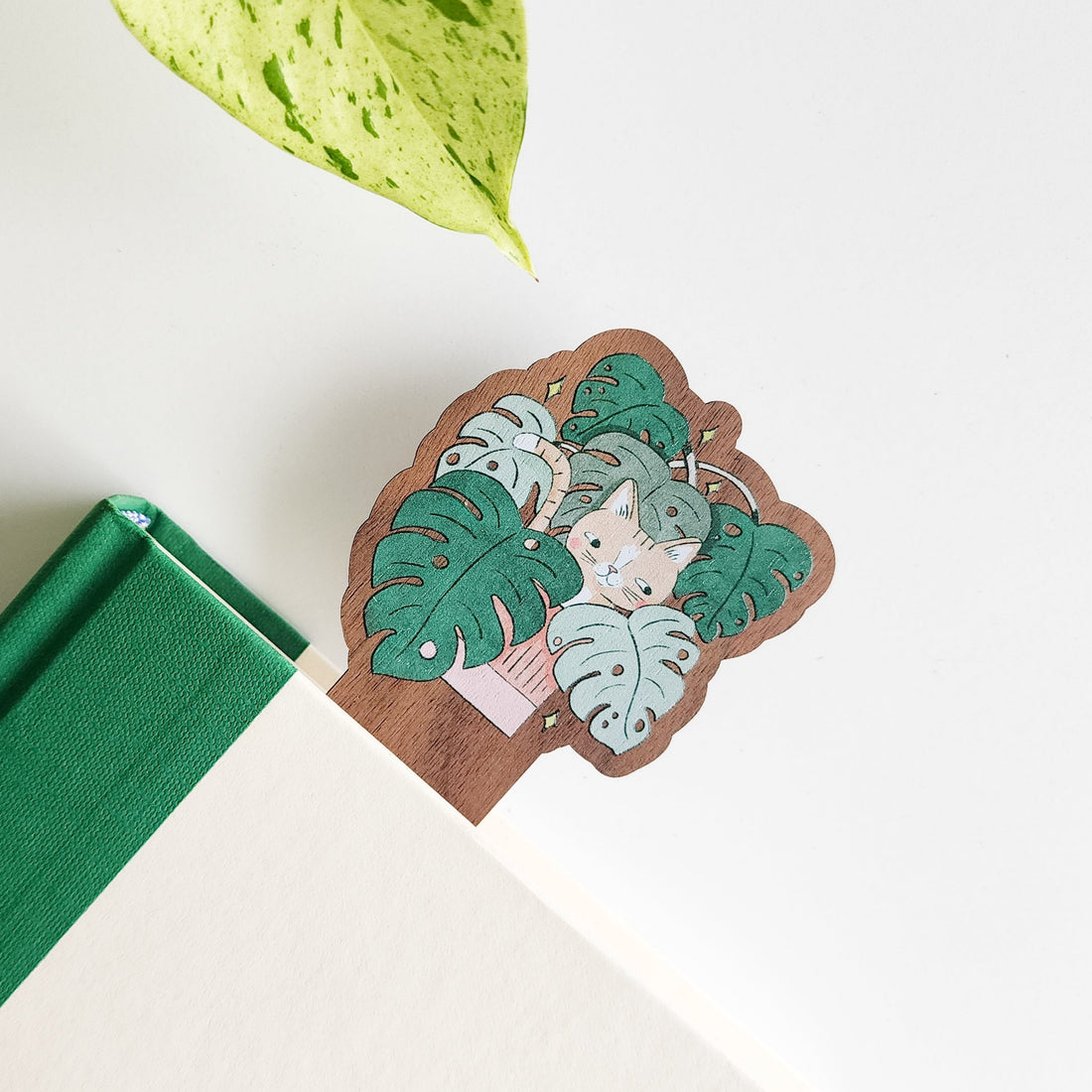 Bookmark with a cat in a monstera plant on a white surface