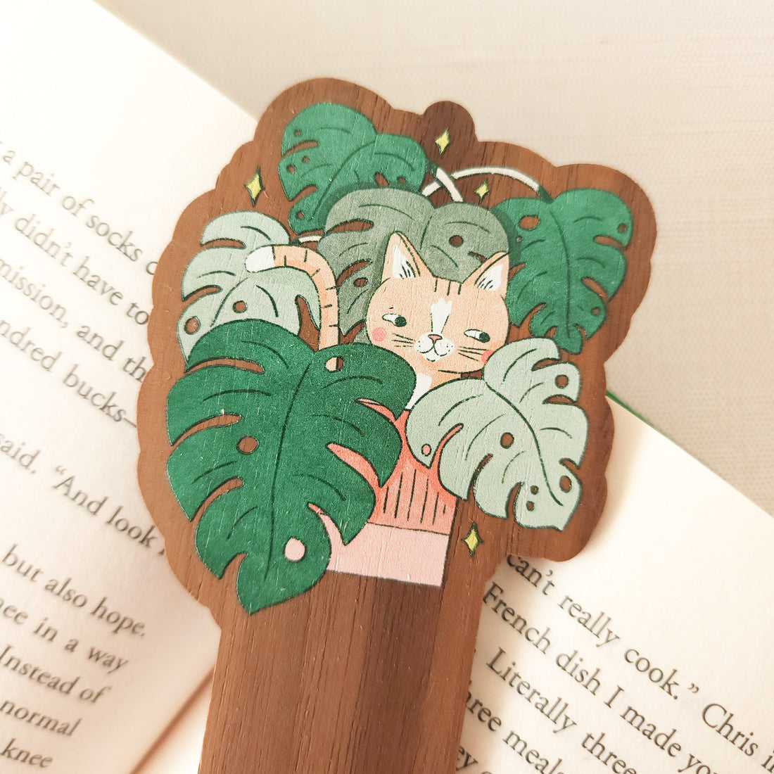 wooden bookmark with an illustration of a cat in a monstera plant sitting on an open book