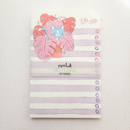 notepad with purple and white stripes and an illustration of a cat in a monstera plant and the words to do
