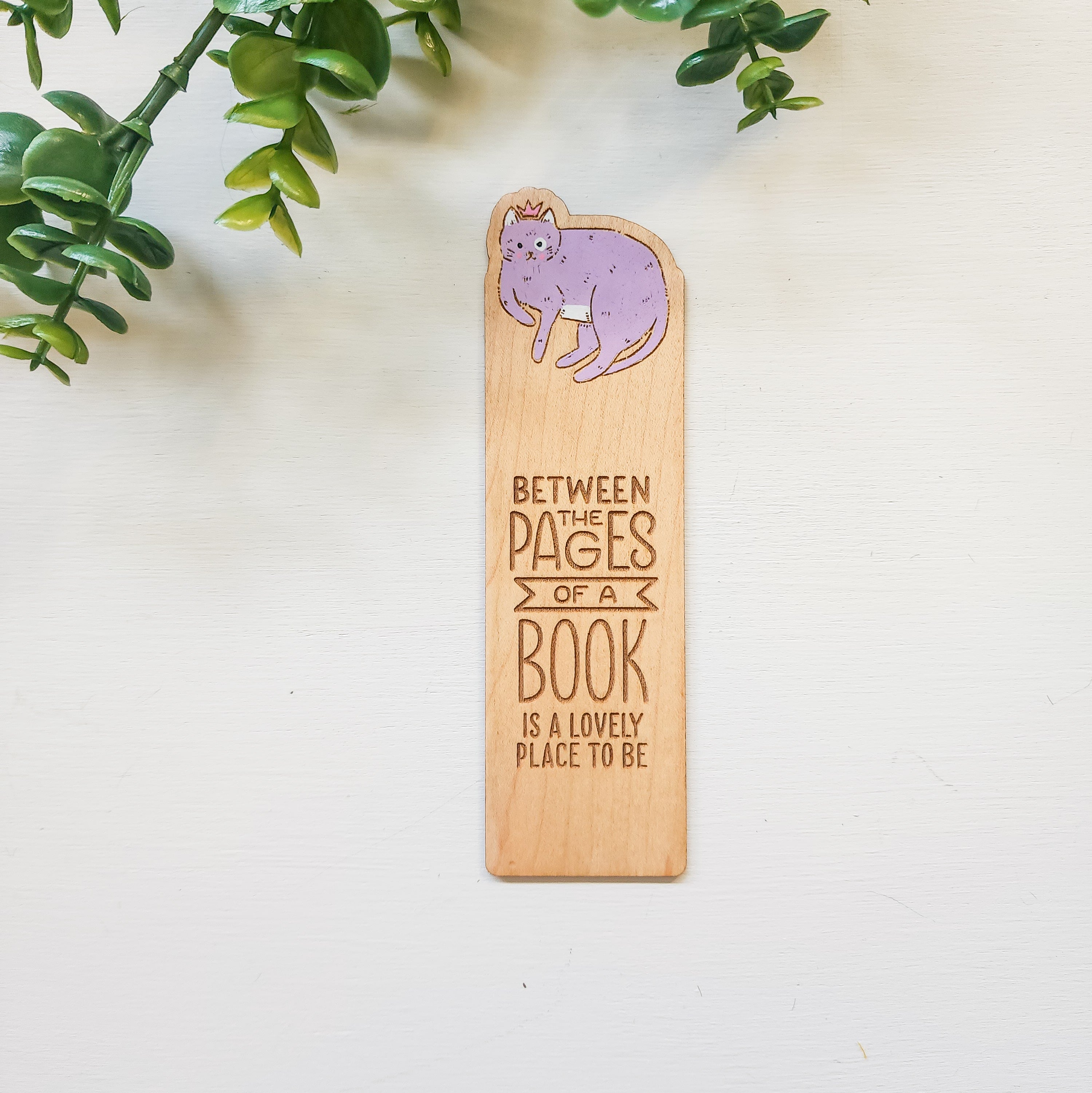 bookmark with a purple cat and the words between the pages of a book is a lovely place to be engraved