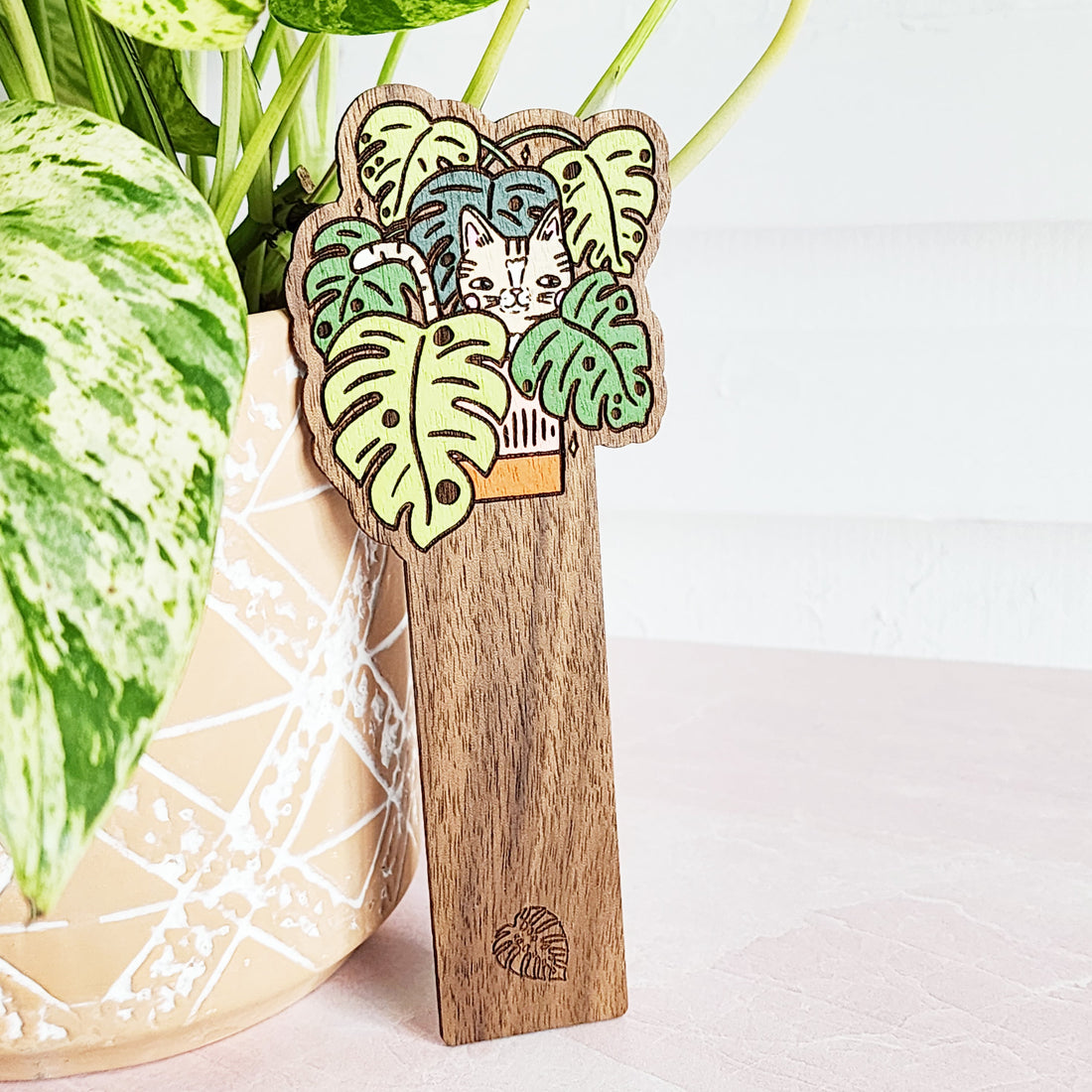 cat bookmark leaning against a plant on a pink table