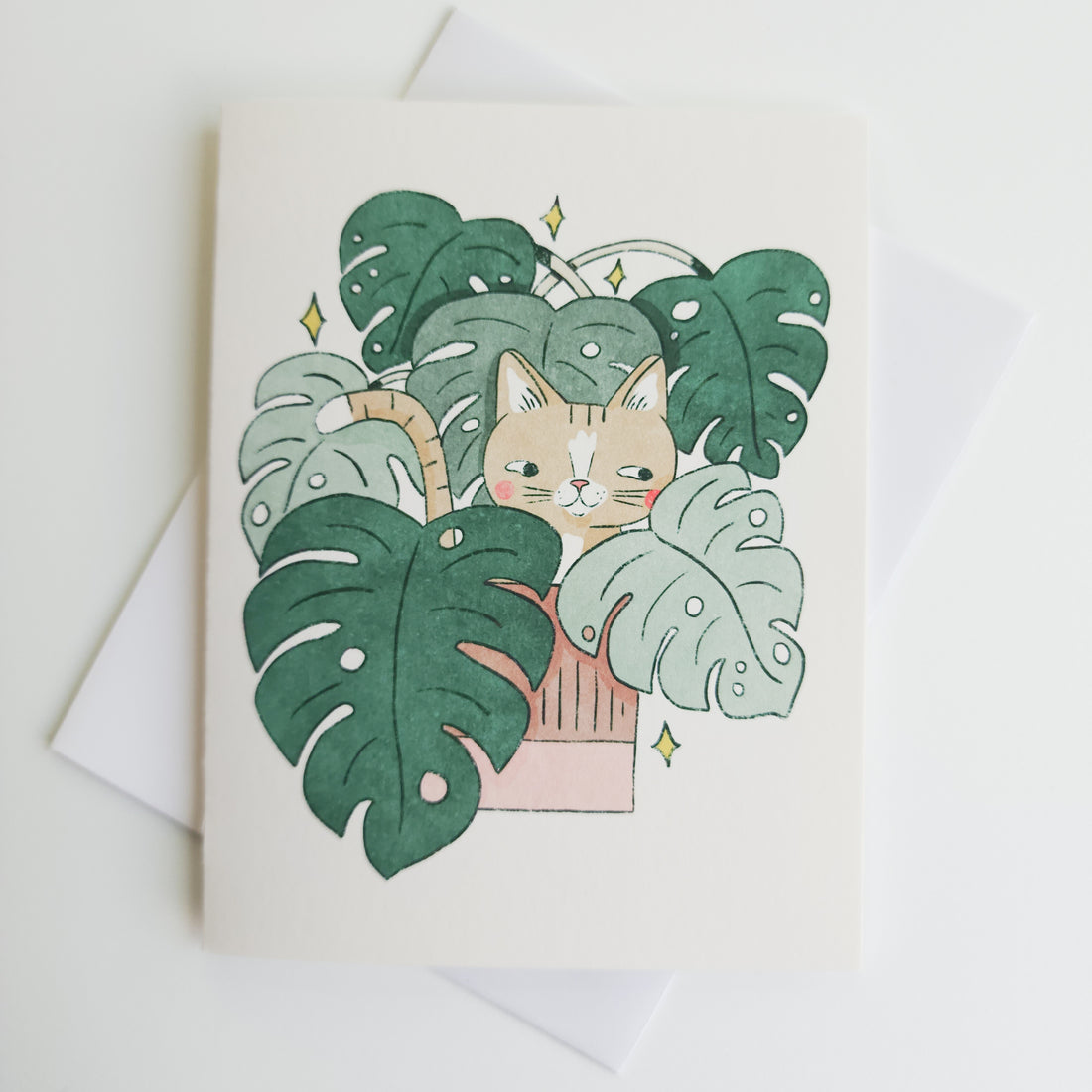 greeting card with an illustrated image of a cat sitting inside a monstera plant