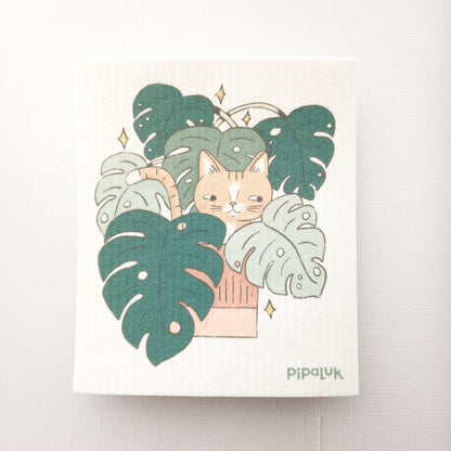 swedish dishcloth with an illustration of a cat in a monstera plant and  pipaluk logo in the bottom right corner
