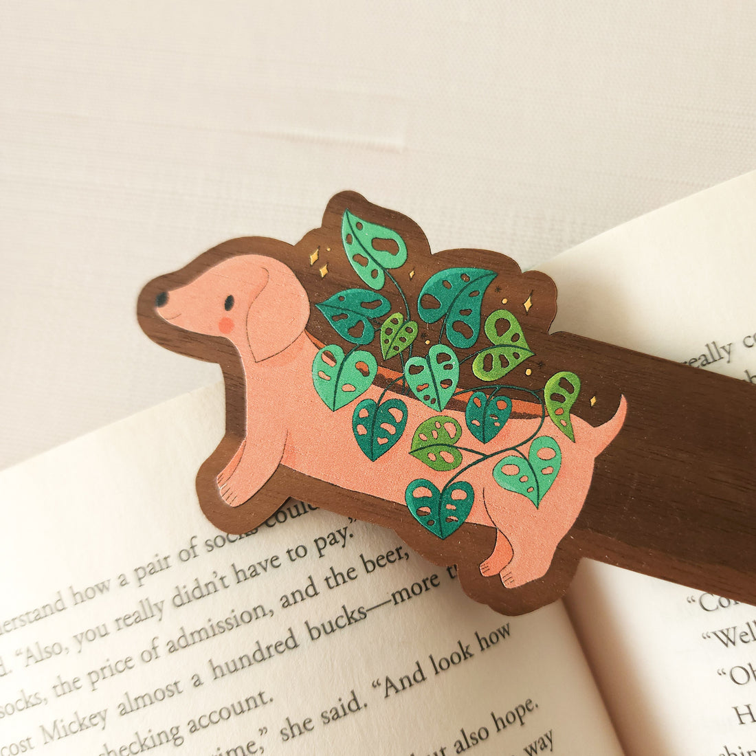 wooden bookmark with an illustration of a dachshund planter with a cheese plant sitting on an open book