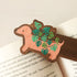 wooden bookmark with an illustration of a dachshund planter with a cheese plant sitting on an open book