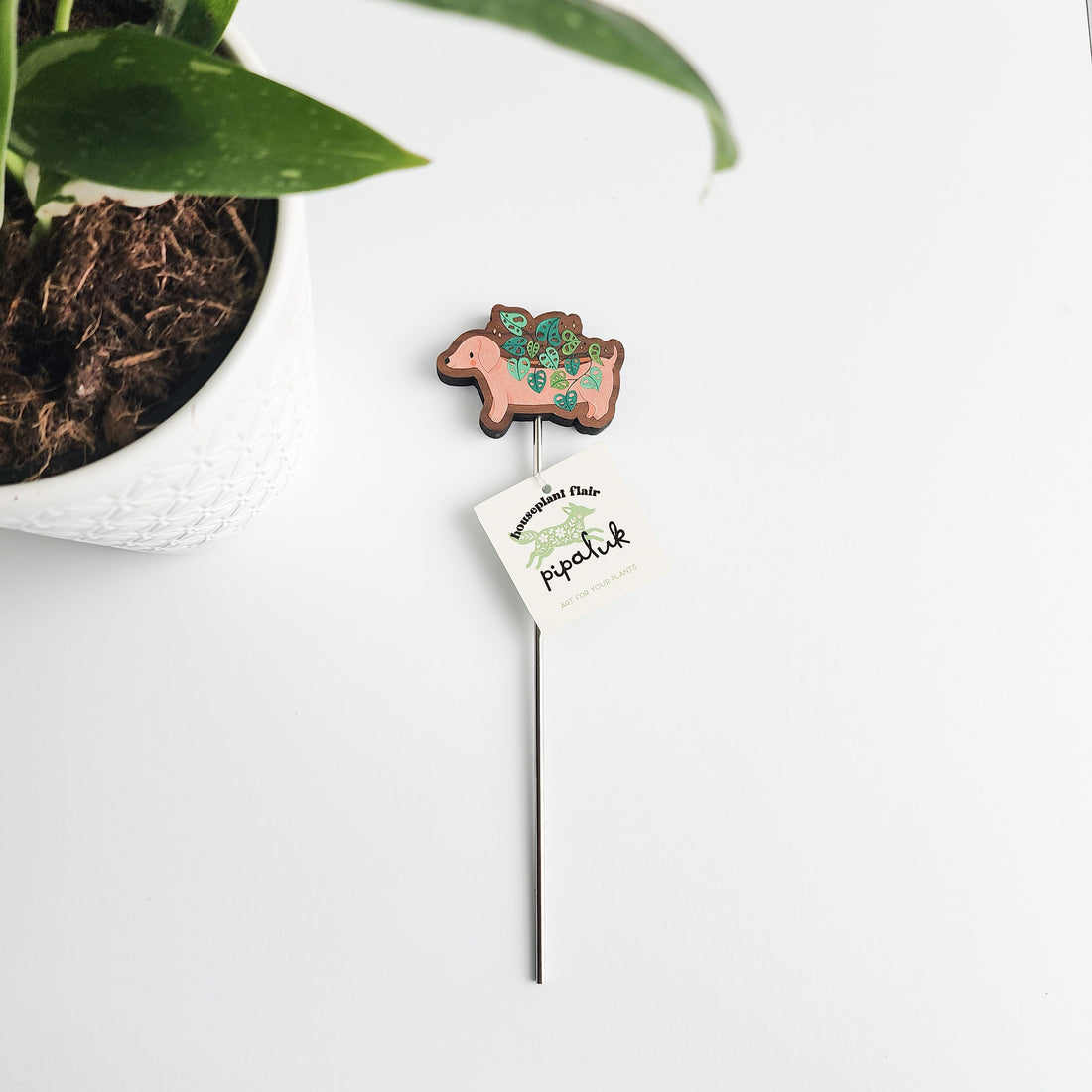 Decorative plant stake with a dachshund design next to a potted plant on a white surface