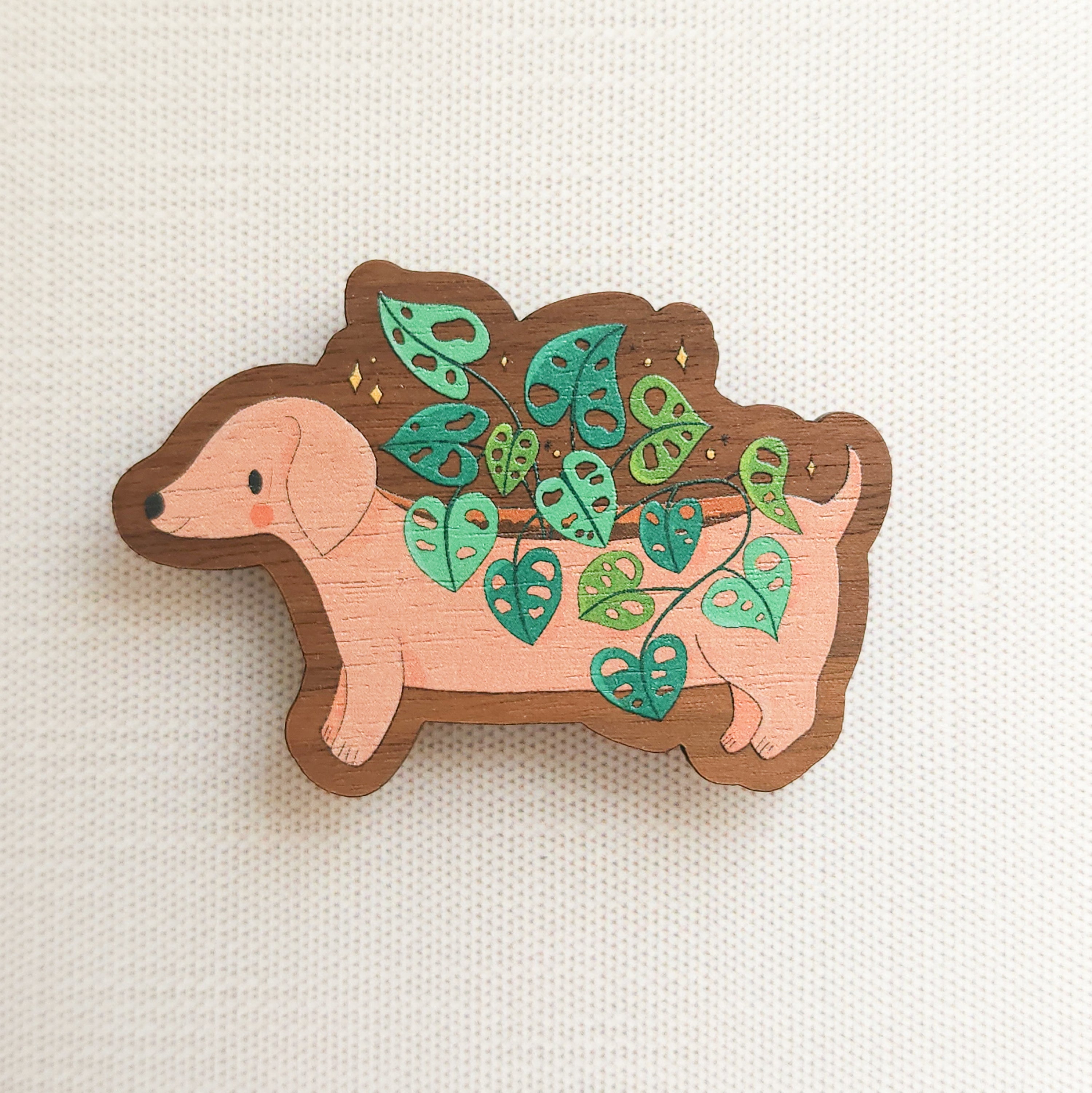 wooden magnet with an illustration of a dachshund planter with a cheese plant on a linen background