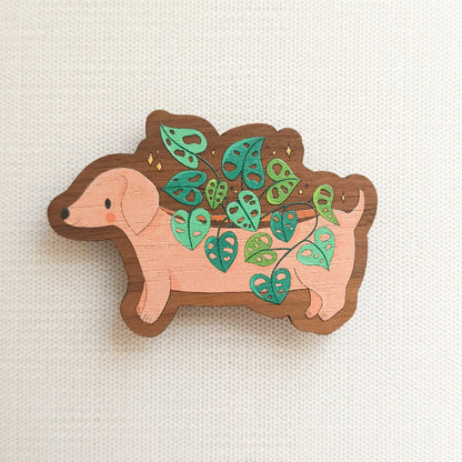 wooden magnet with an illustration of a dachshund planter with a cheese plant on a linen background