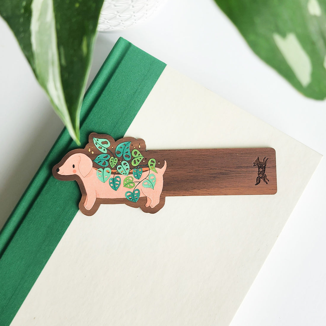 Wooden bookmark with a dachshund design holding leaves, placed on a green book.