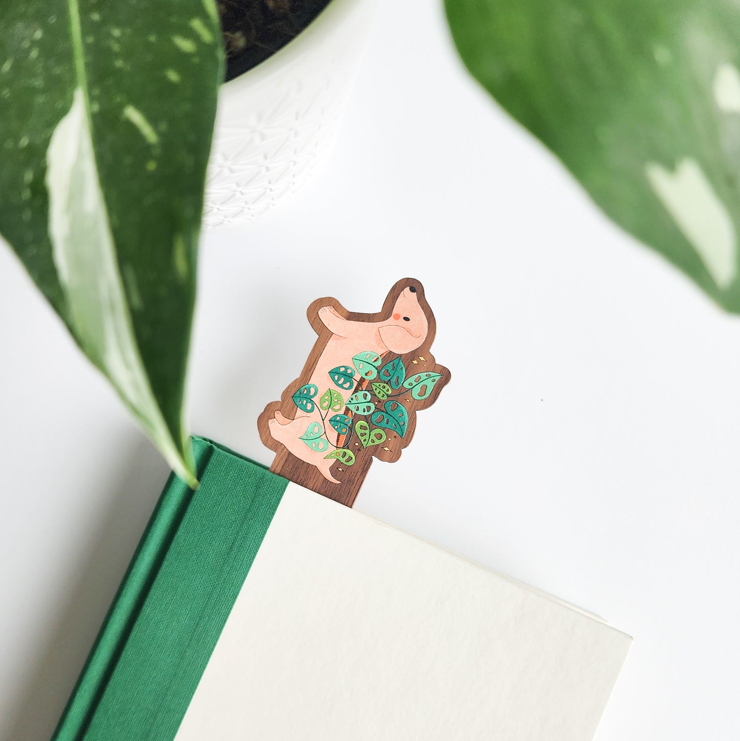 Bookmark with a dog design inside a green book, surrounded by leaves on a light background
