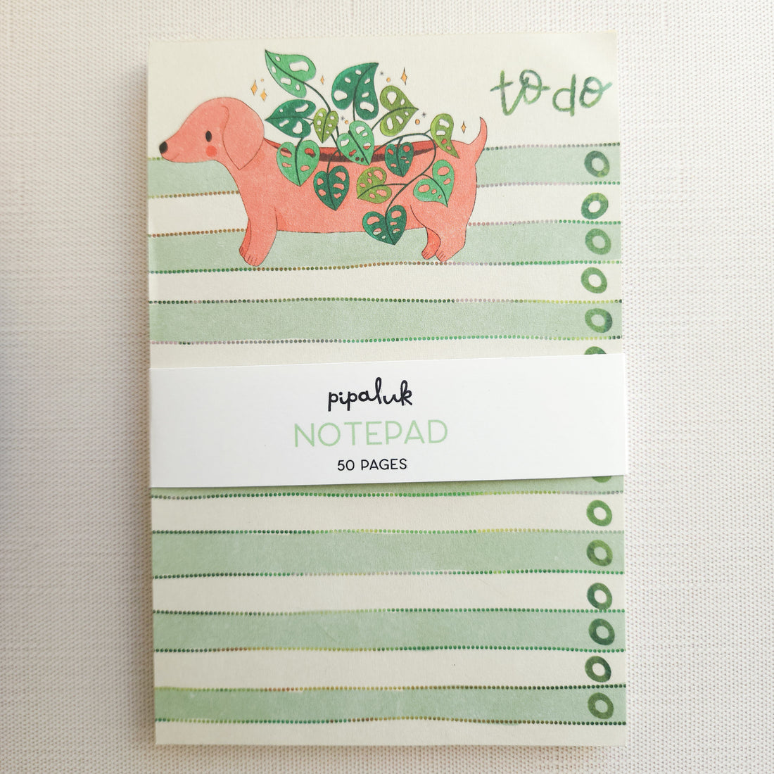 notepad with an illustrated dachshund and green stripes on a neutral background

