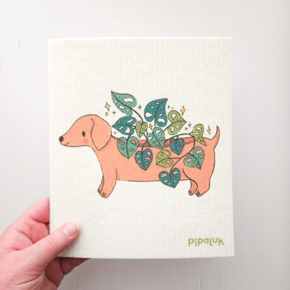 swedish dishcloth with an image of a dachshund planter growing a cheeseplant, held in a hand