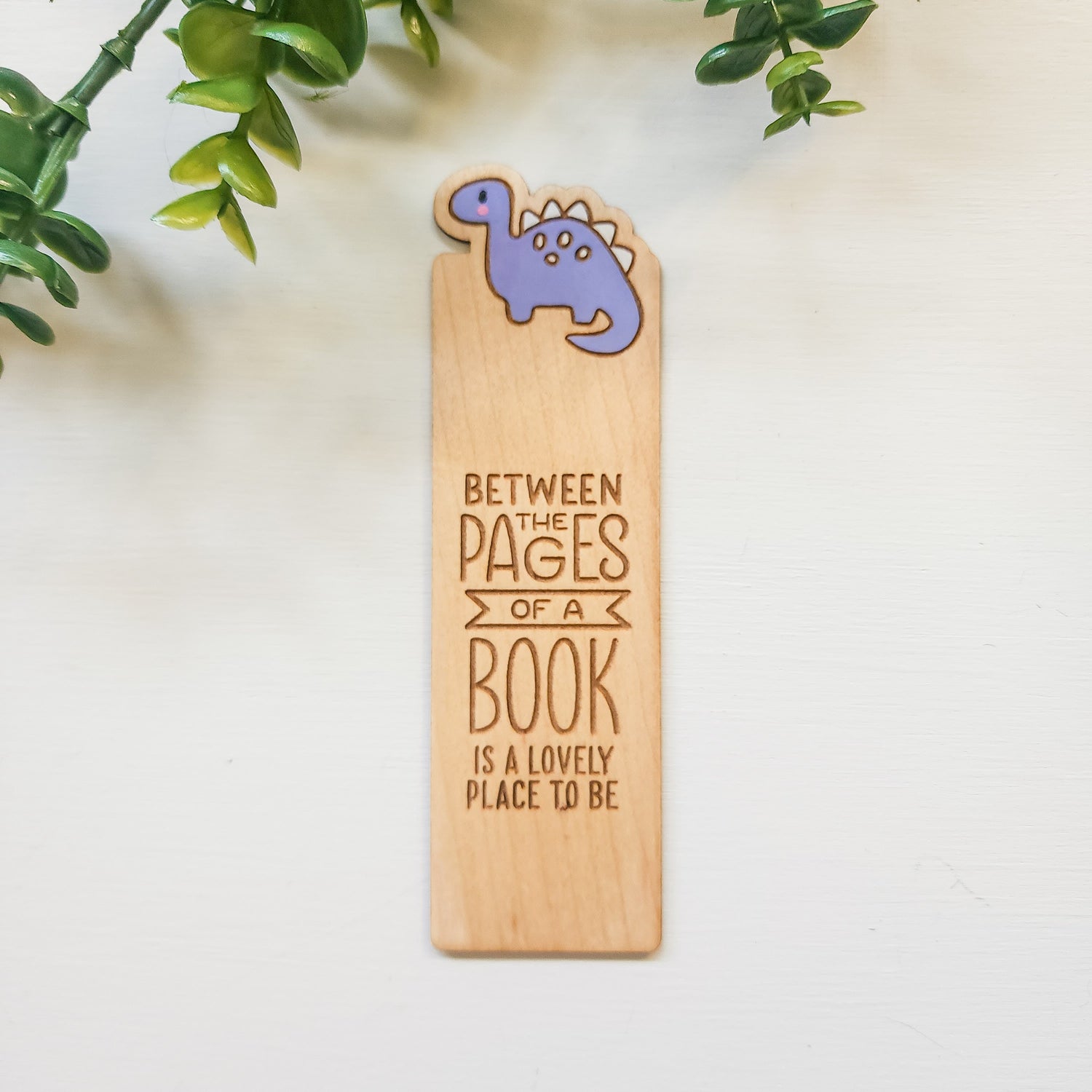 wooden bookmark with a dinosuar and the words between the pages of a book is a lovely place to be engraved