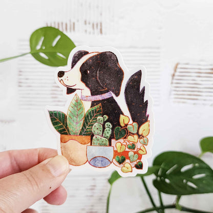 sticker of a black and white dog sitting in front of potted plants