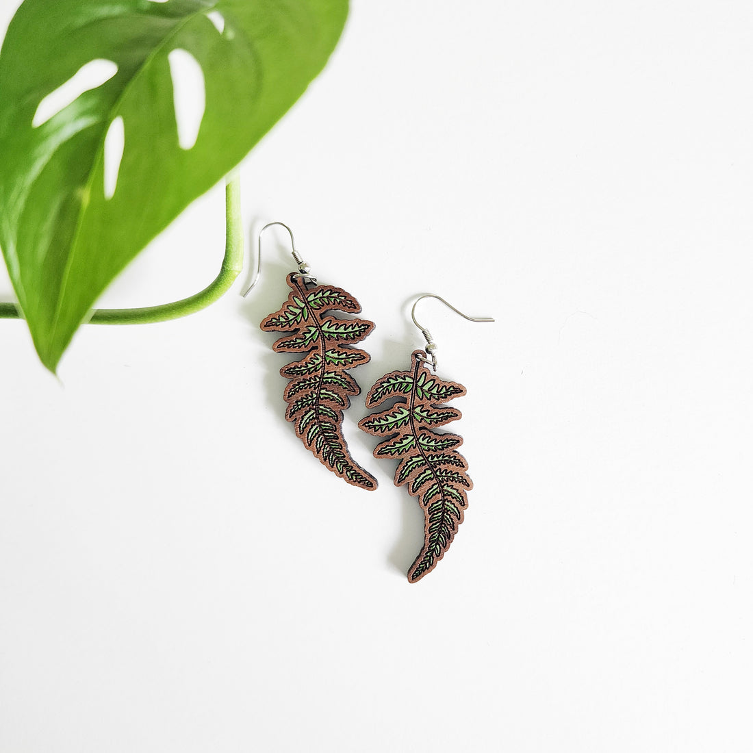 pair of fern leaf earrings on a white background next to a leaf