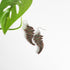 pair of fern leaf earrings on a white background next to a leaf