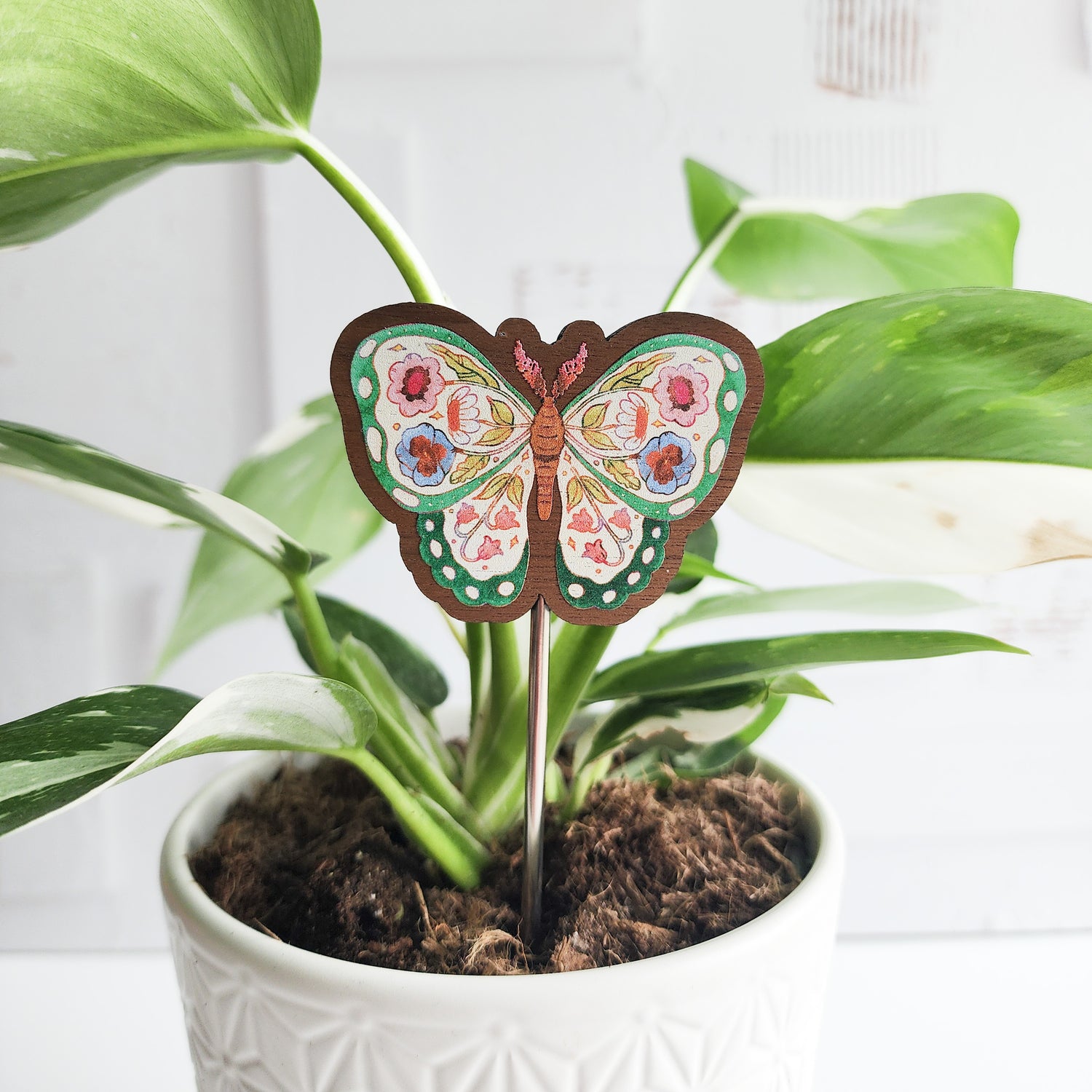 Decorative butterfly plant stake in a pot with green leaves