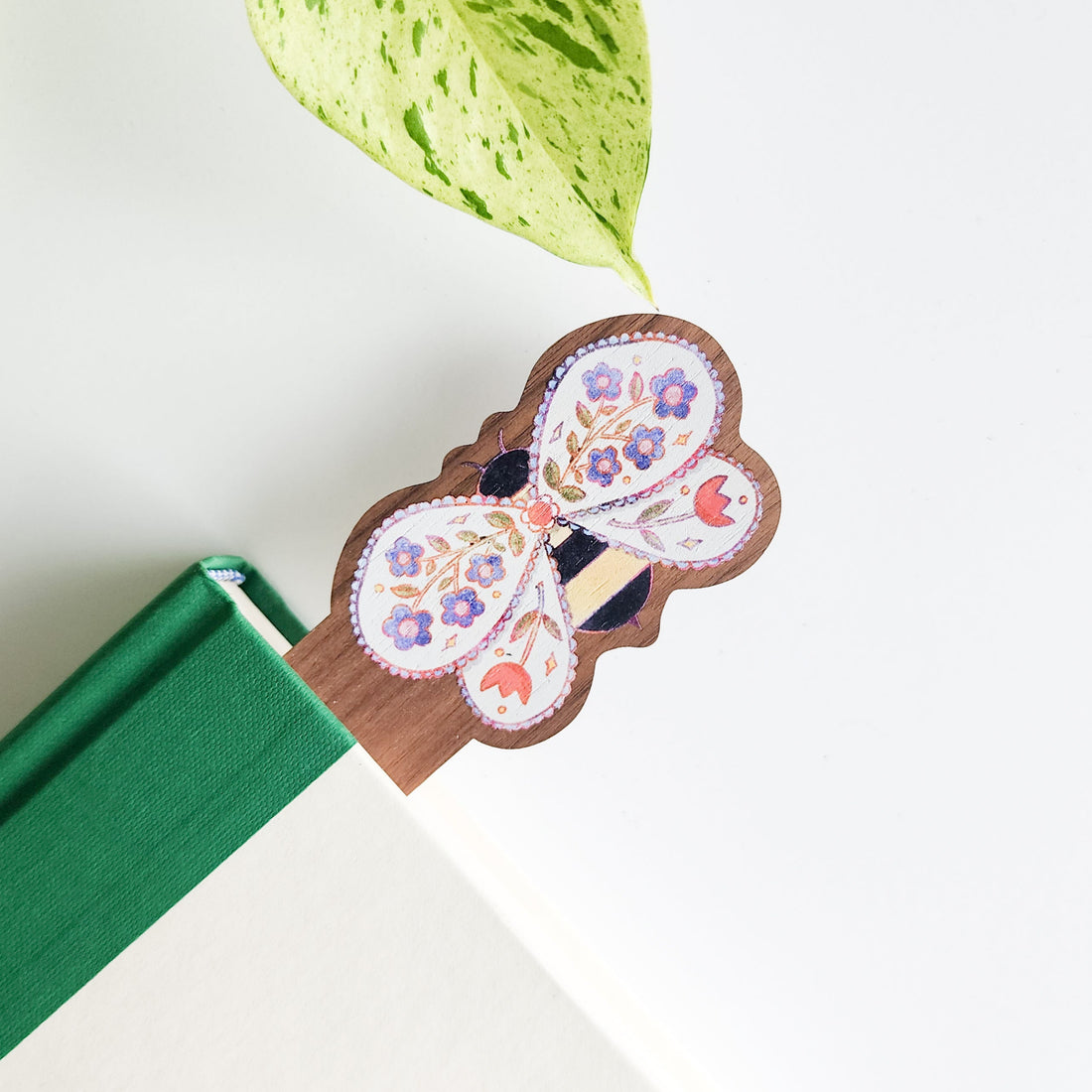 bee-shaped wooden bookmark with floral design on a green book