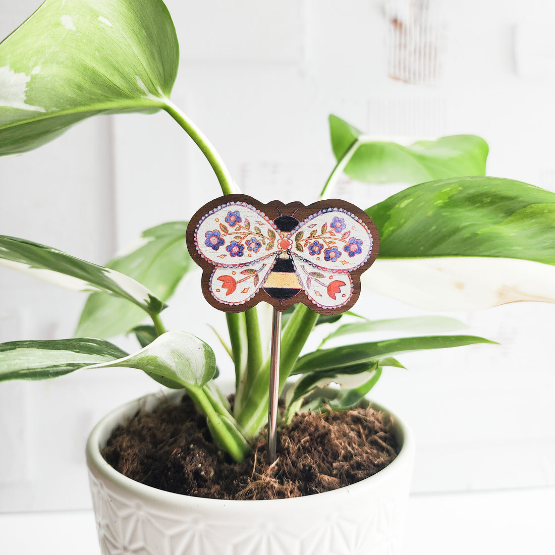 a bee plant pick inside a potted plant against a white brick background