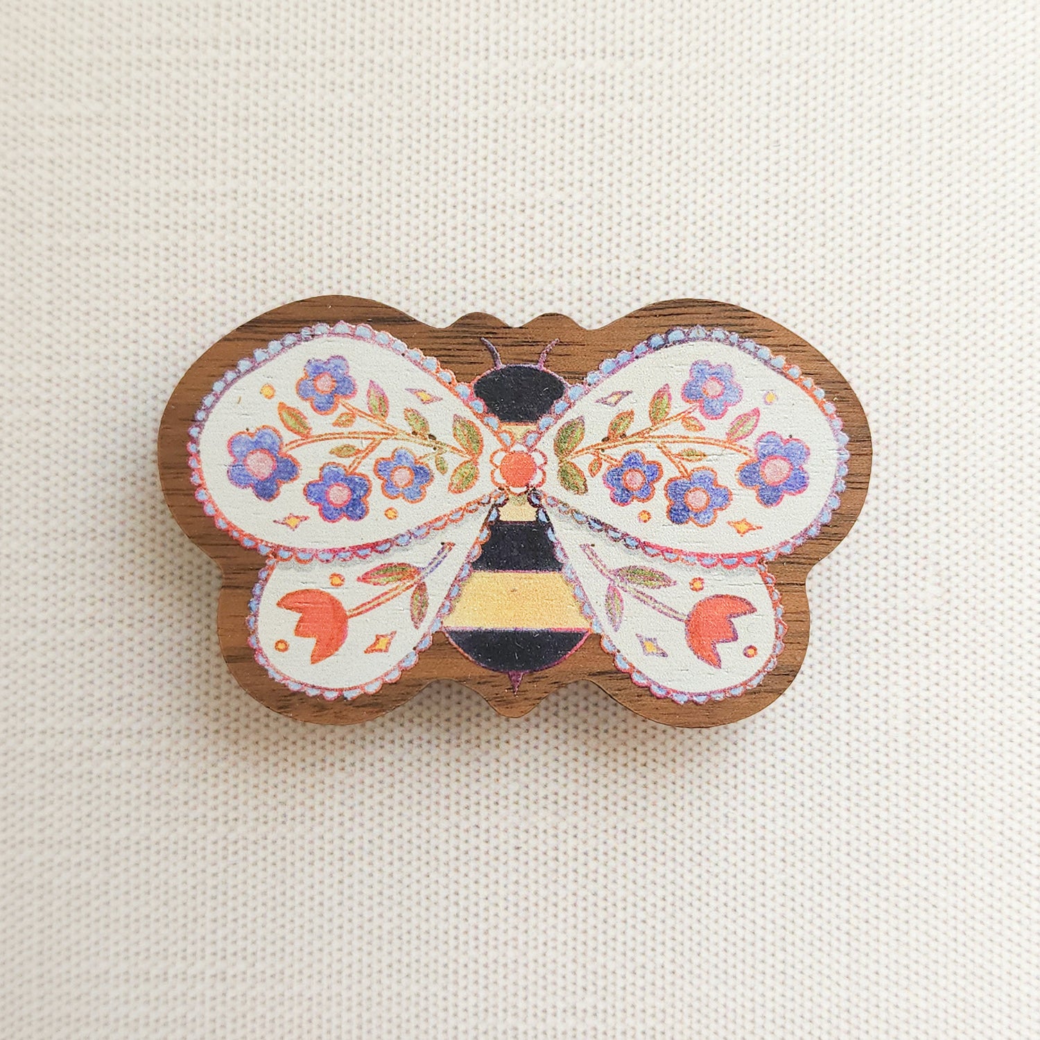 wooden magnet with an illustration of a bee with flowers in its wings on a linen background