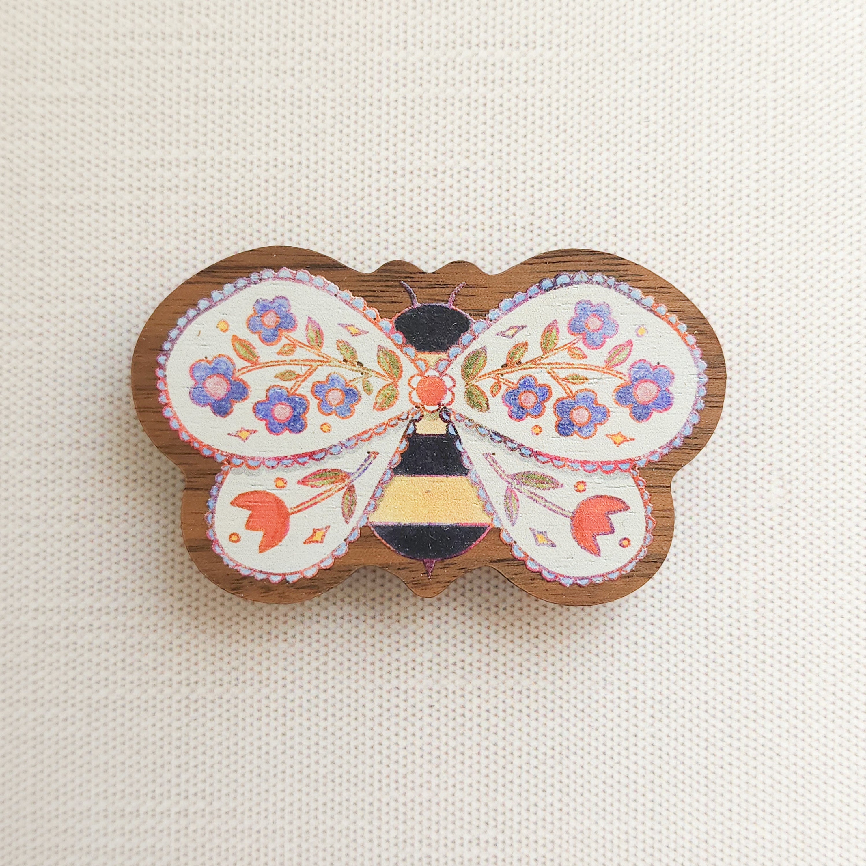wooden magnet with an illustration of a bee with flowers in its wings on a linen background