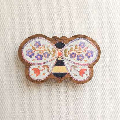 wooden magnet with an illustration of a bee with flowers in its wings on a linen background