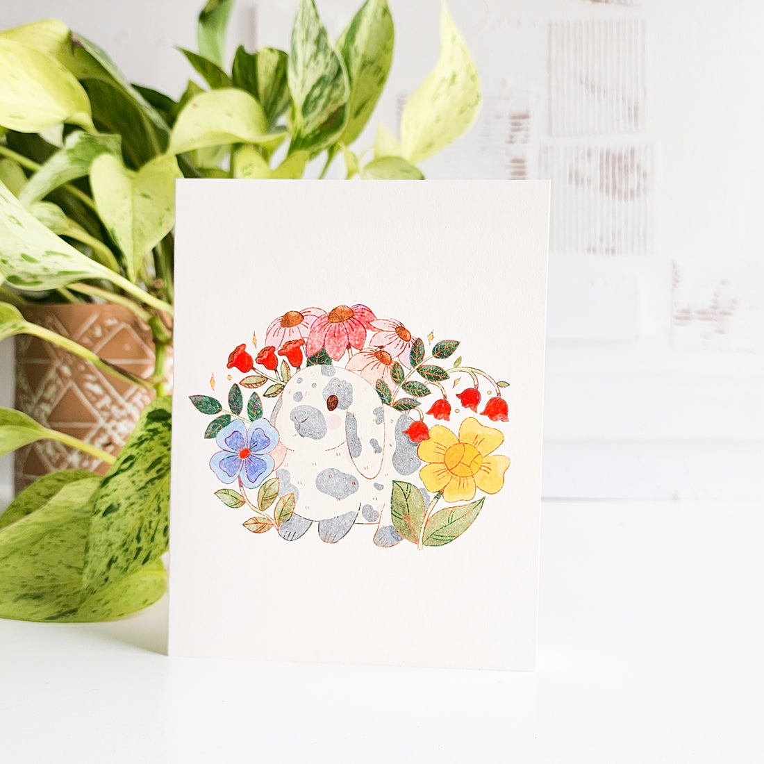 Card with floral design and a rabbit on a white background with plants in the background