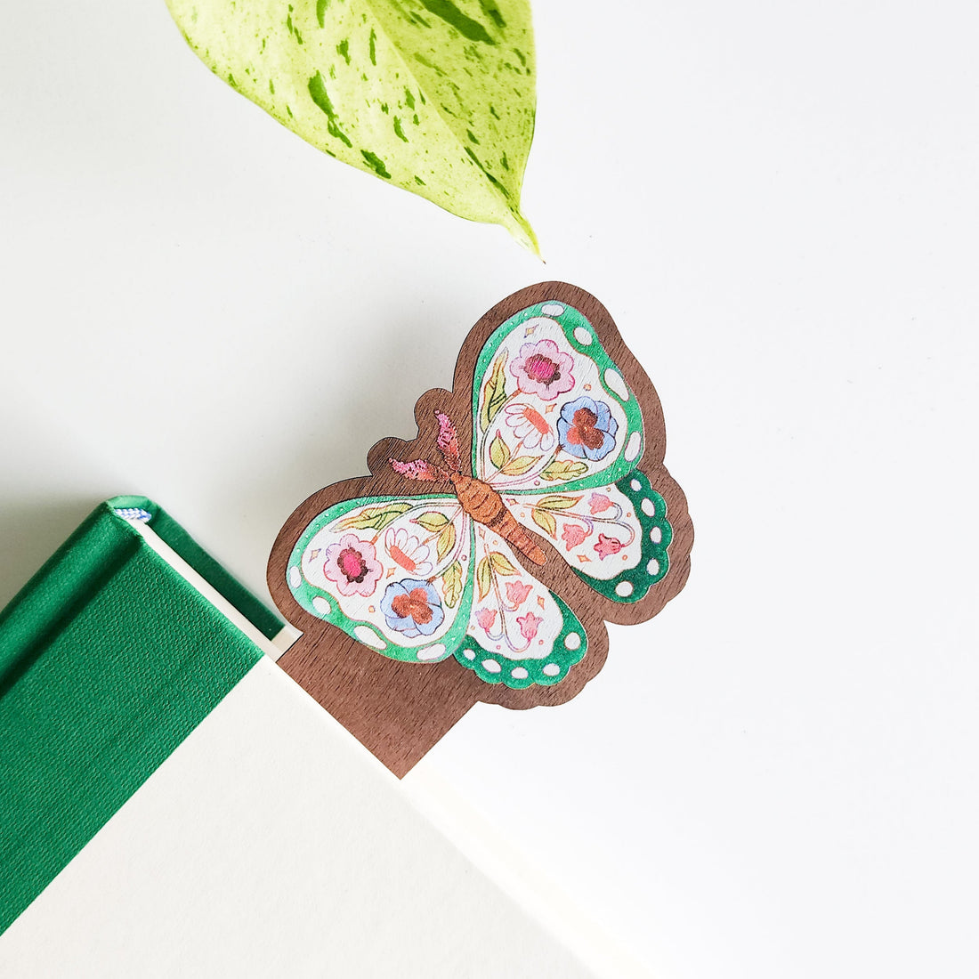 Butterfly-shaped bookmark with floral design on a green book with leaves in the background